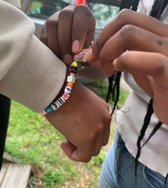 En mörkhyad flicka sätter ett armband på en annan flickas arm.