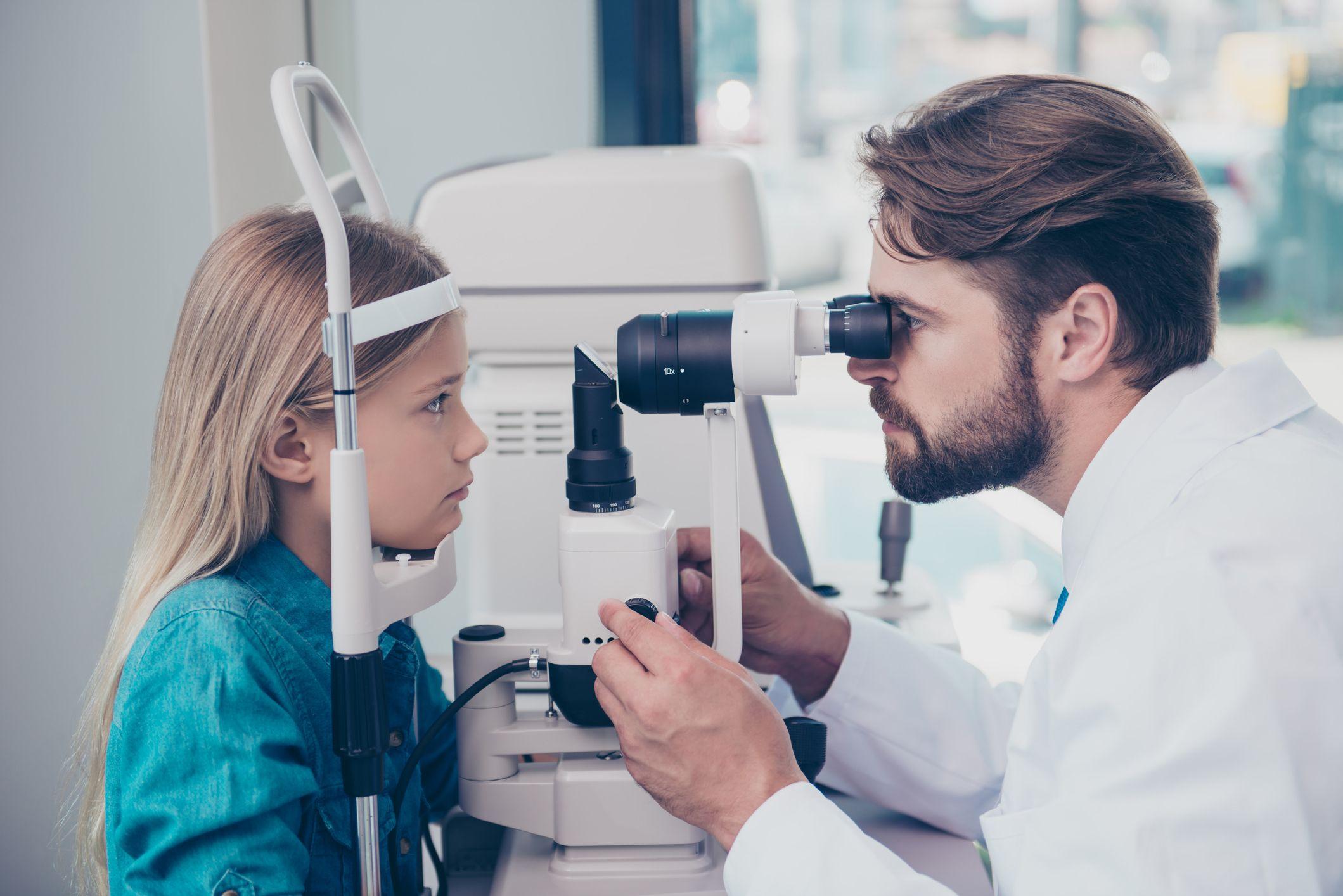 En doktor undersöker en flickas ögon med hjälp av ett mikroskop.