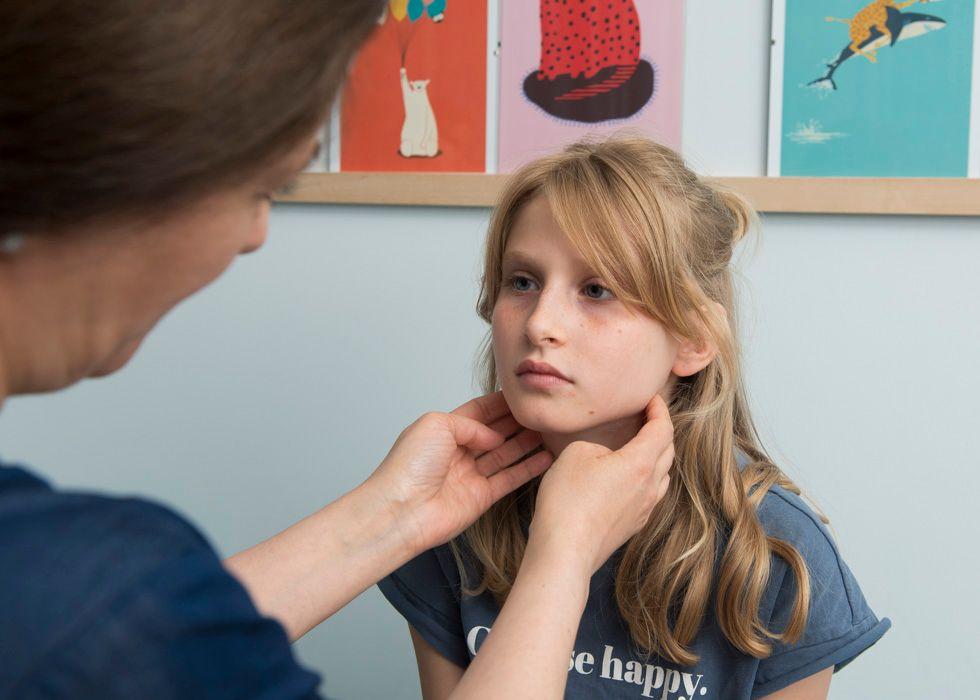 En kvinnlig doktor undersöker lymfkörtlarna på halsen på en flicka med långt, ljust hår.