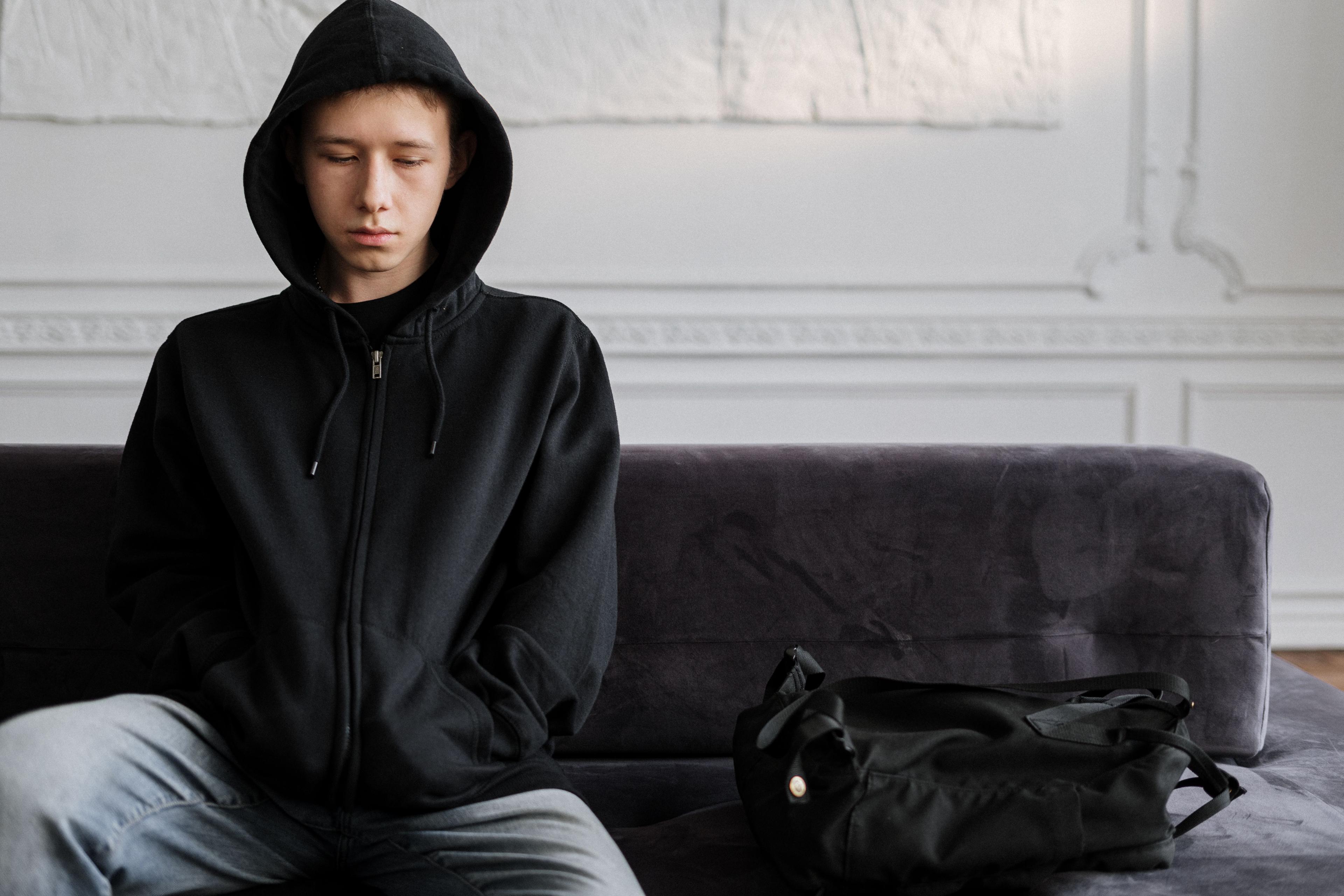Tonårskille i svart hoodie sitter i en svart soffa. Han ser ledsen ut.