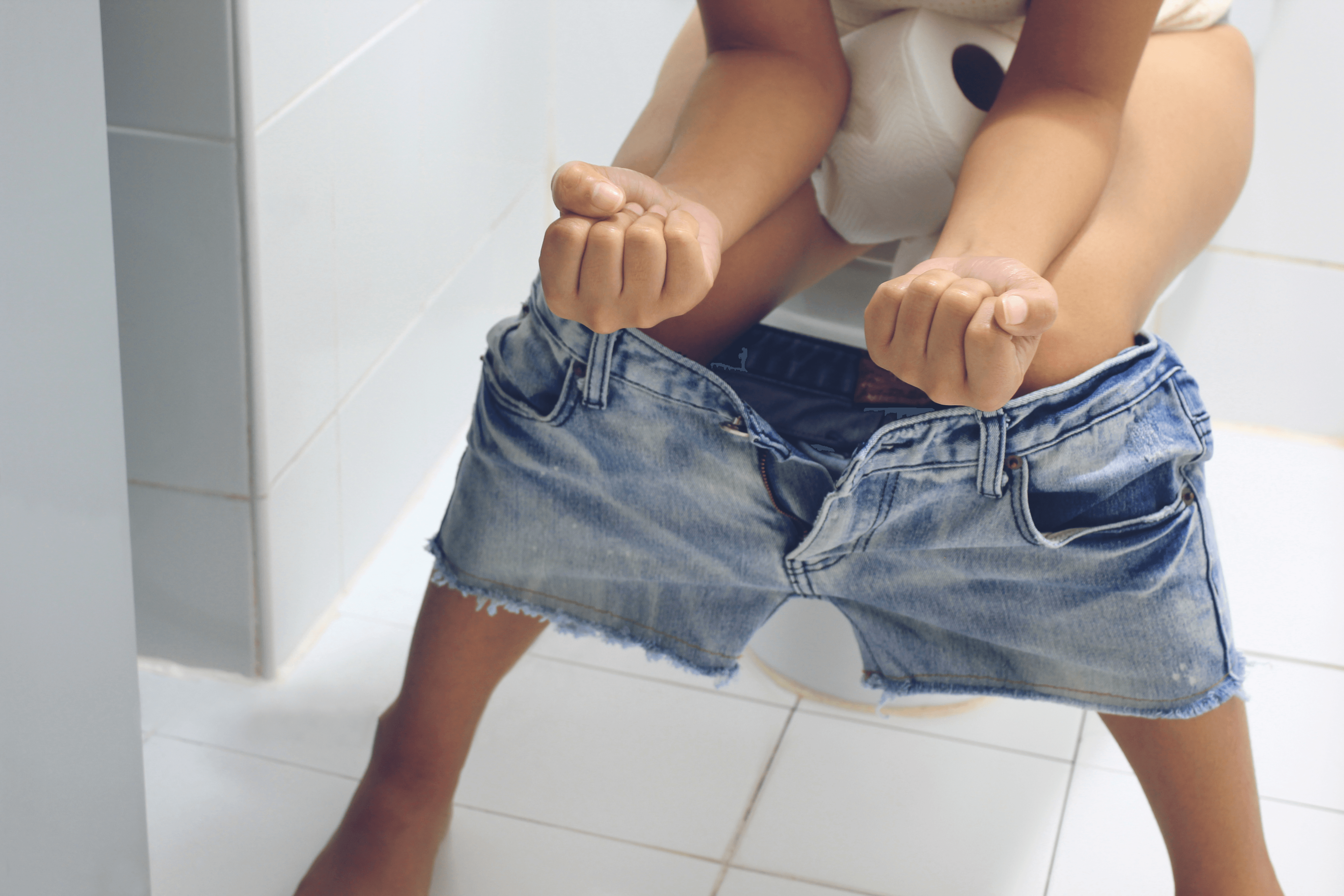 Barn i jeansshorts som sitter på en toalett.