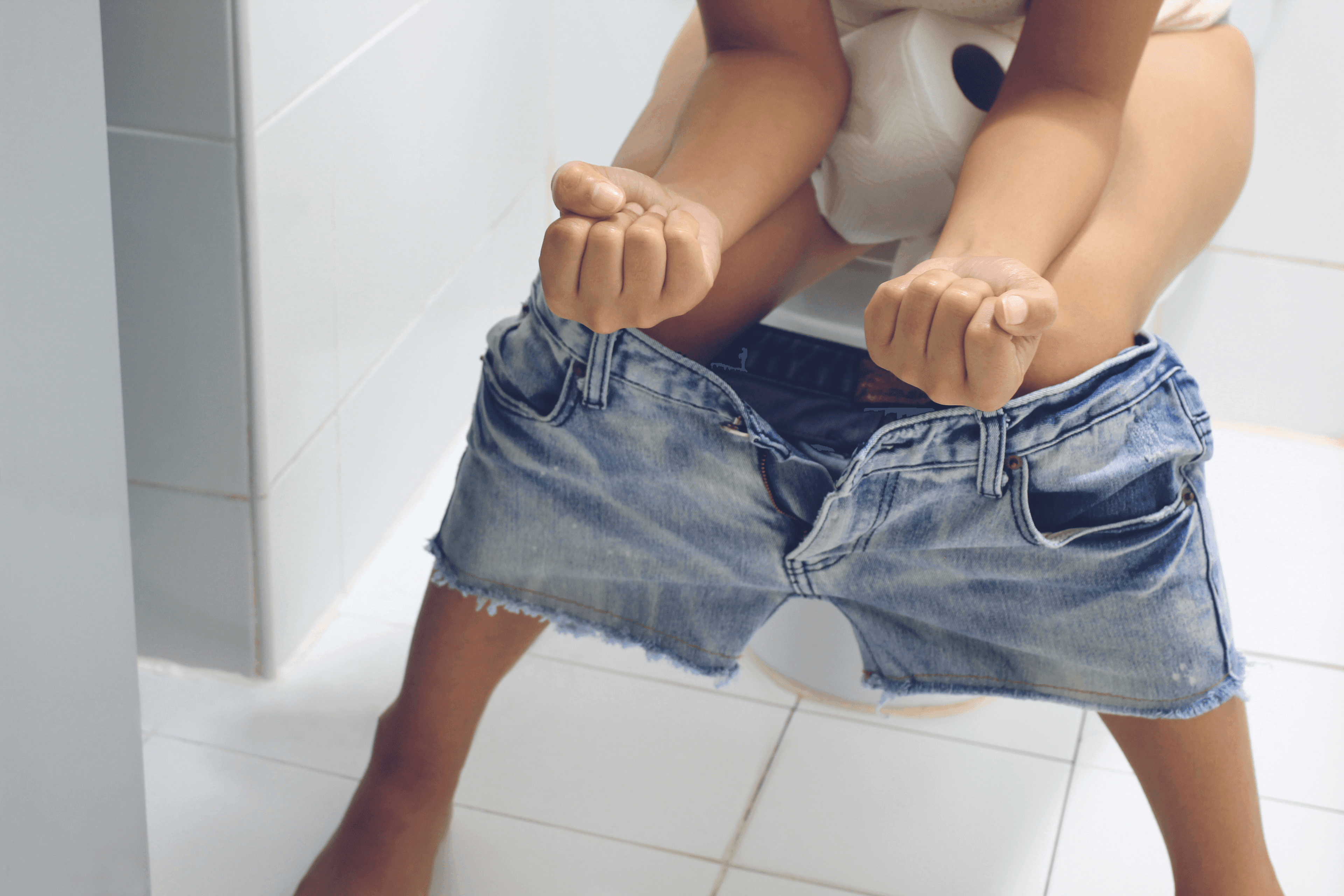Child with jeans shorts sitting on a toilet.