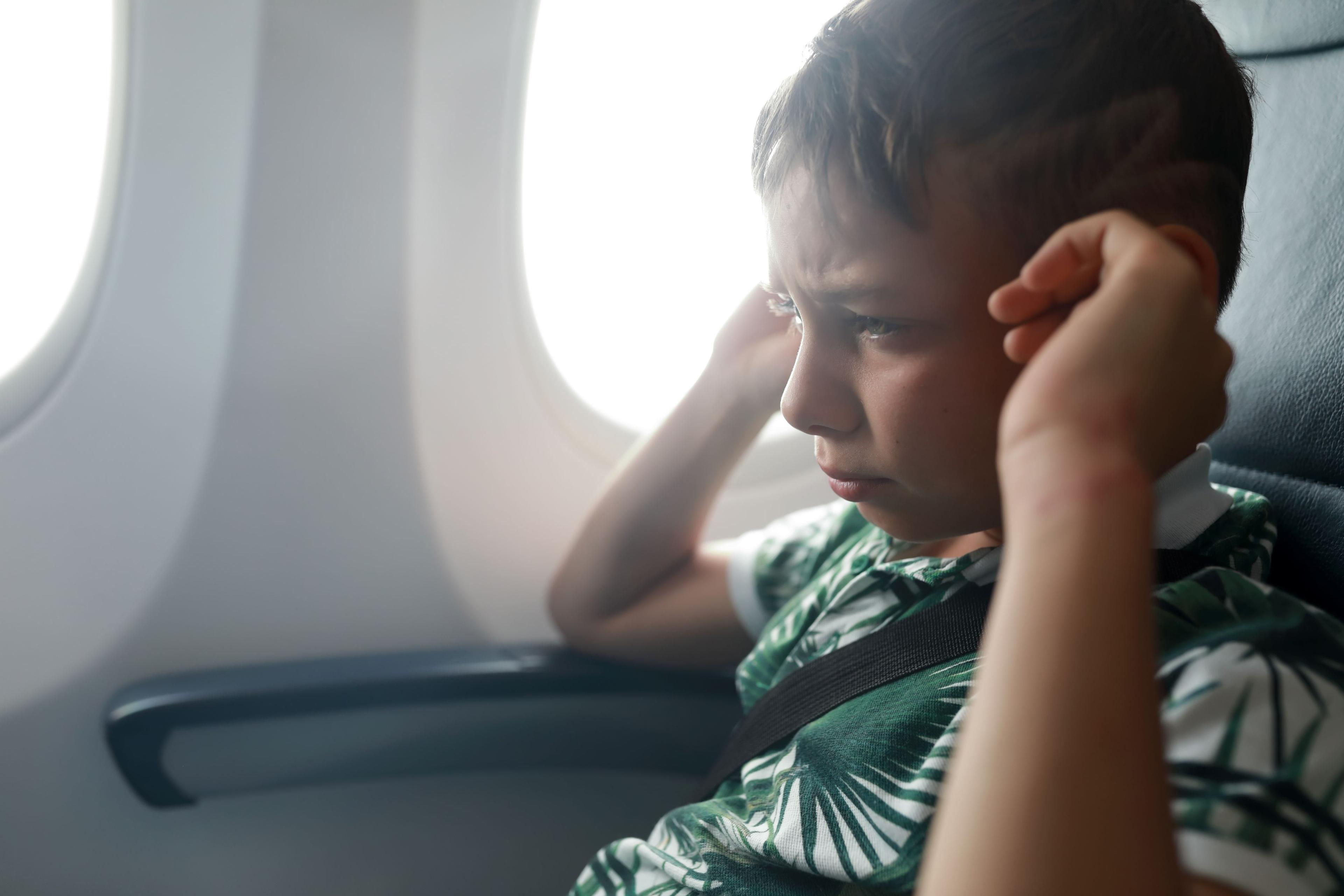 Pojke i en grön-vit t-shirt i ett flygplan. Håller sig för öronen.