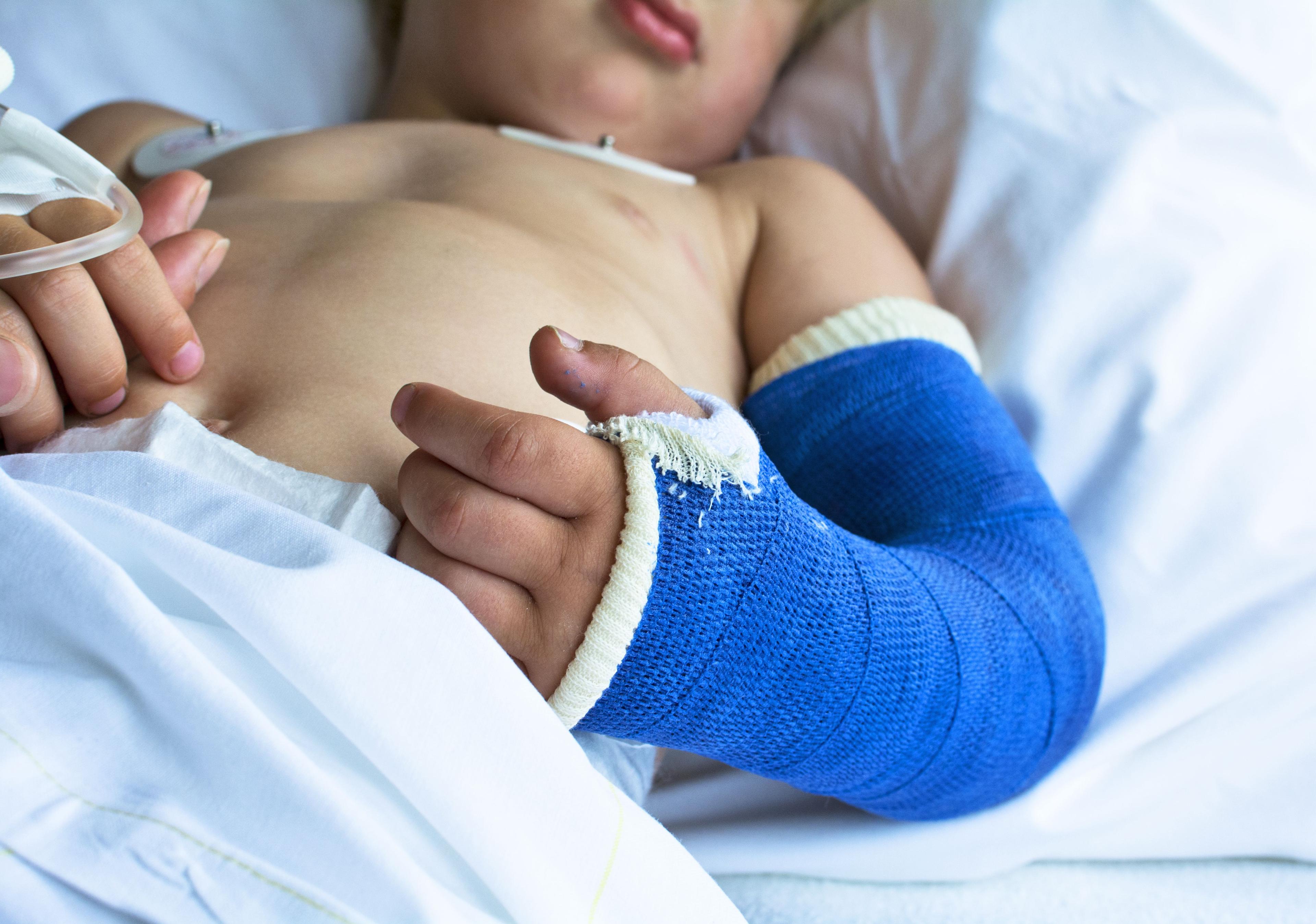 Pojke med blått gips på armen ligger i en säng.