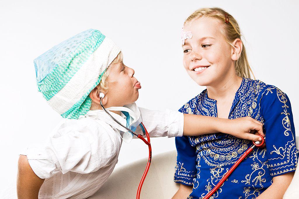 En pojke i en grön operationsmössa leker doktor. Han lyssnar på hjärtat på en kompis.