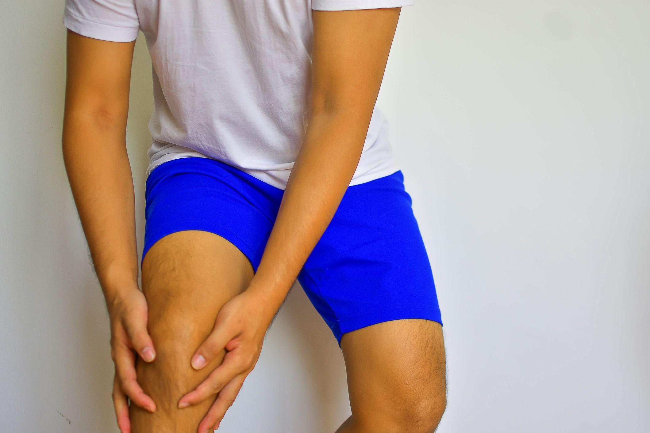 En tonårskille i blå träningsshorts och vit t-shirt håller sina händer omkring sitt böjda knä.