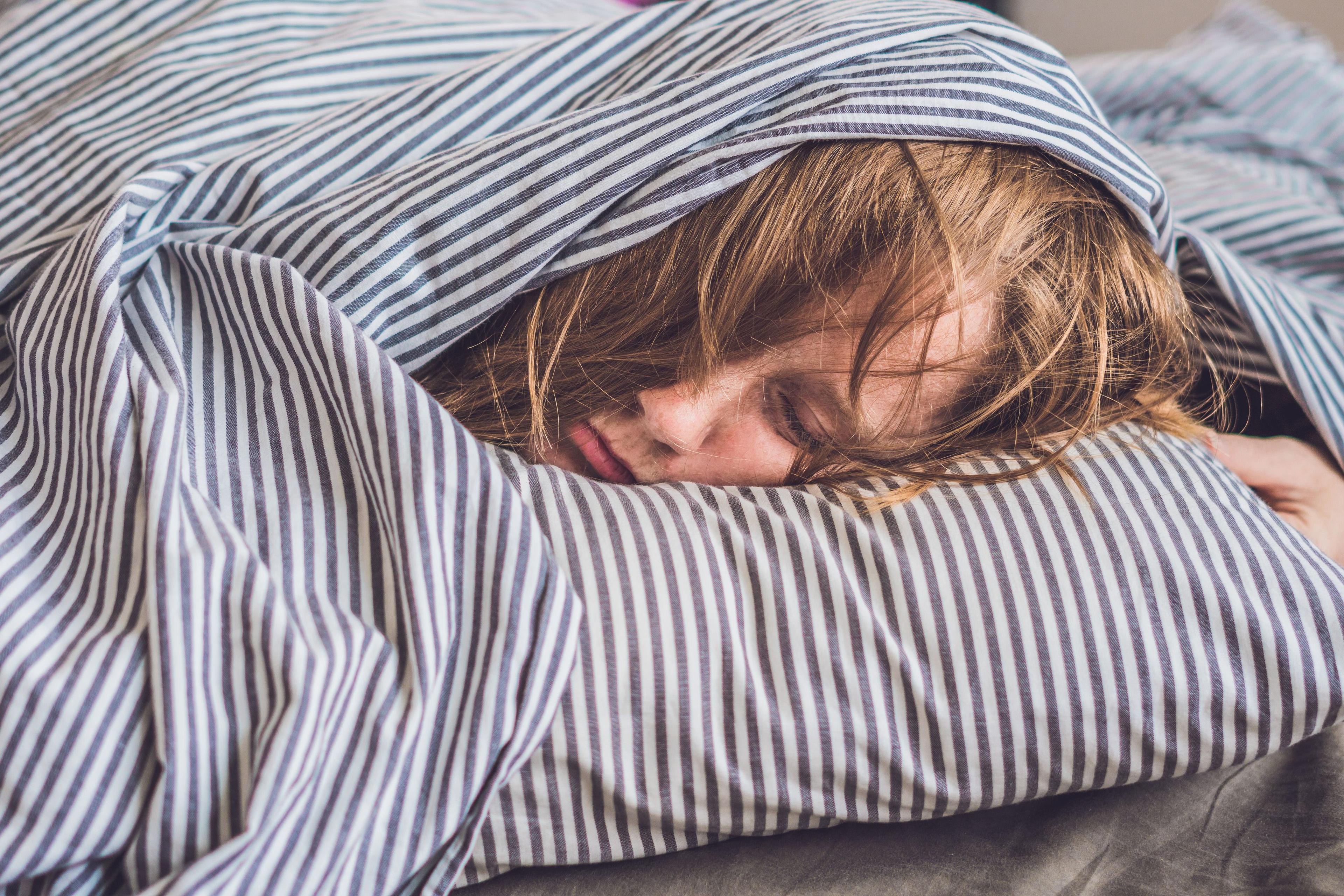 Tonåring sover med täcket över huvudet.