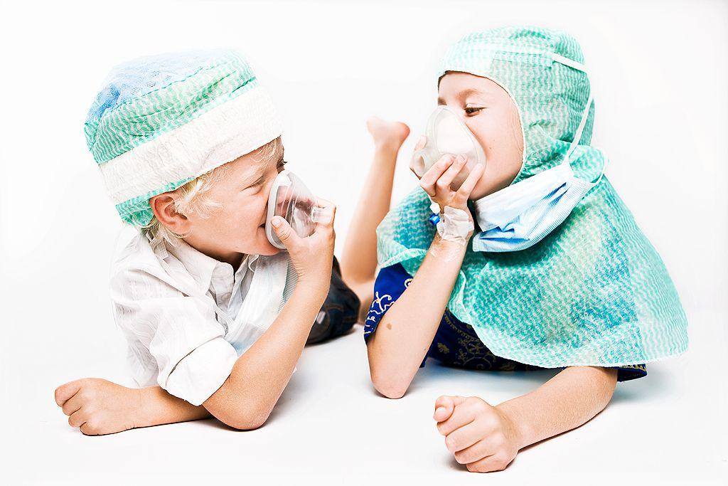 Girl and boy in scrub caps lie on their stomachs, each breathing in an oxygen mask.