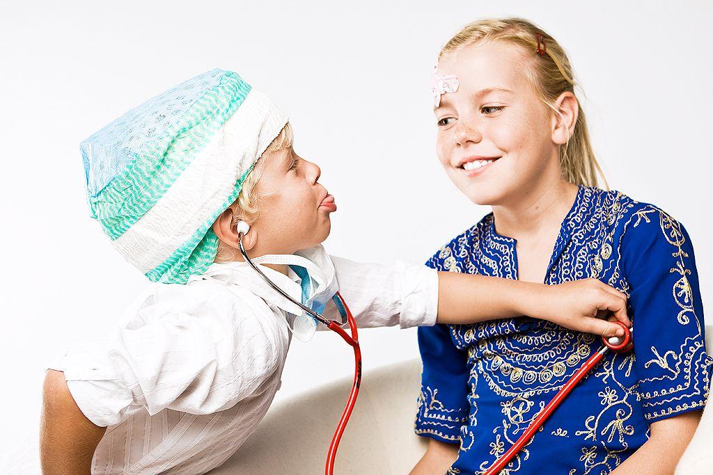 A boy is listening to a girl's heart with a red stethoscope.