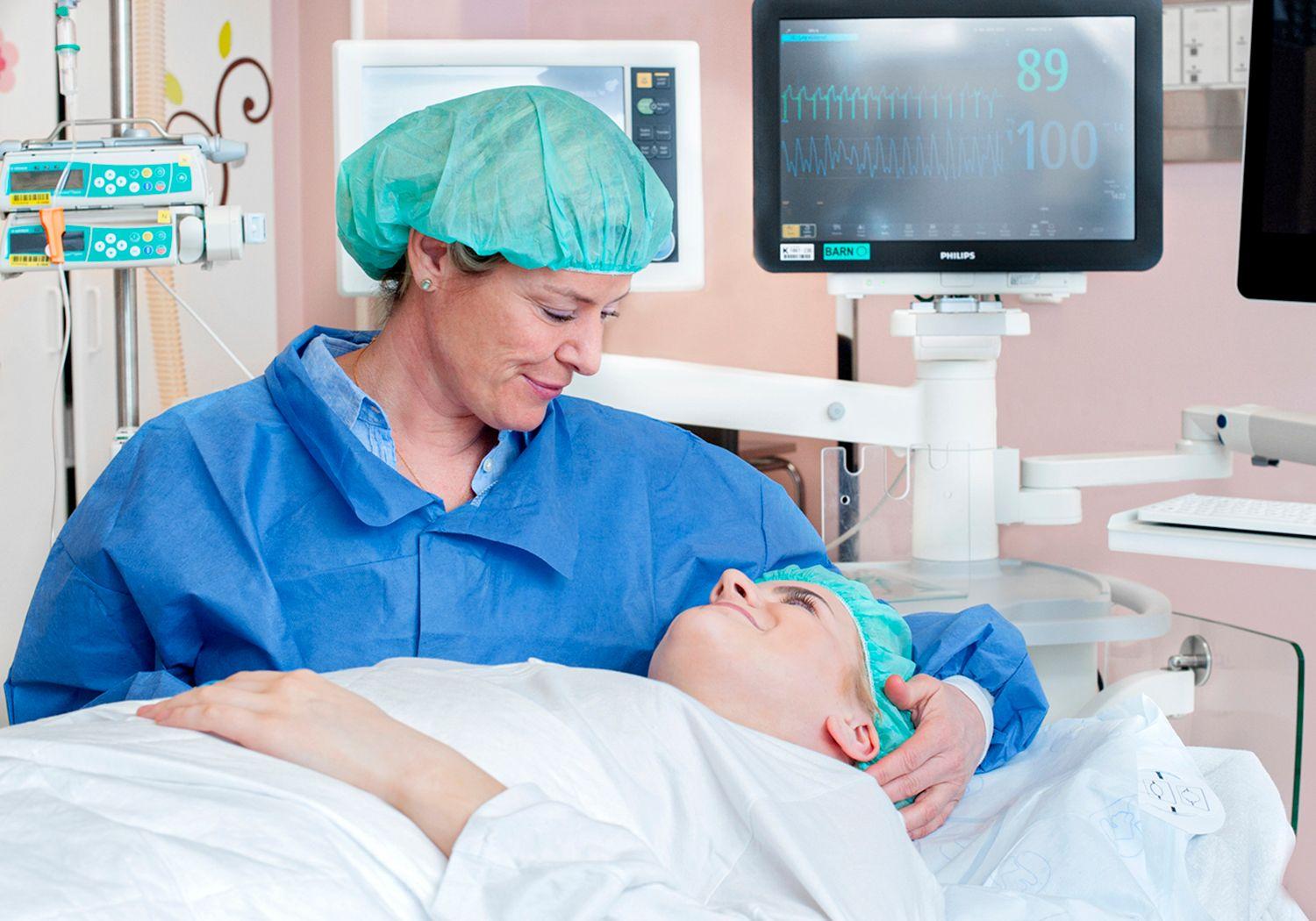Teenage girl lying on an operating table. Her mother is beside the bed wearing scrubs and scrub cap.