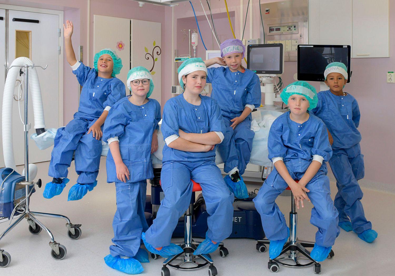 Operationsklädda barn i en operationssal. Alla med olika mössor på sig.