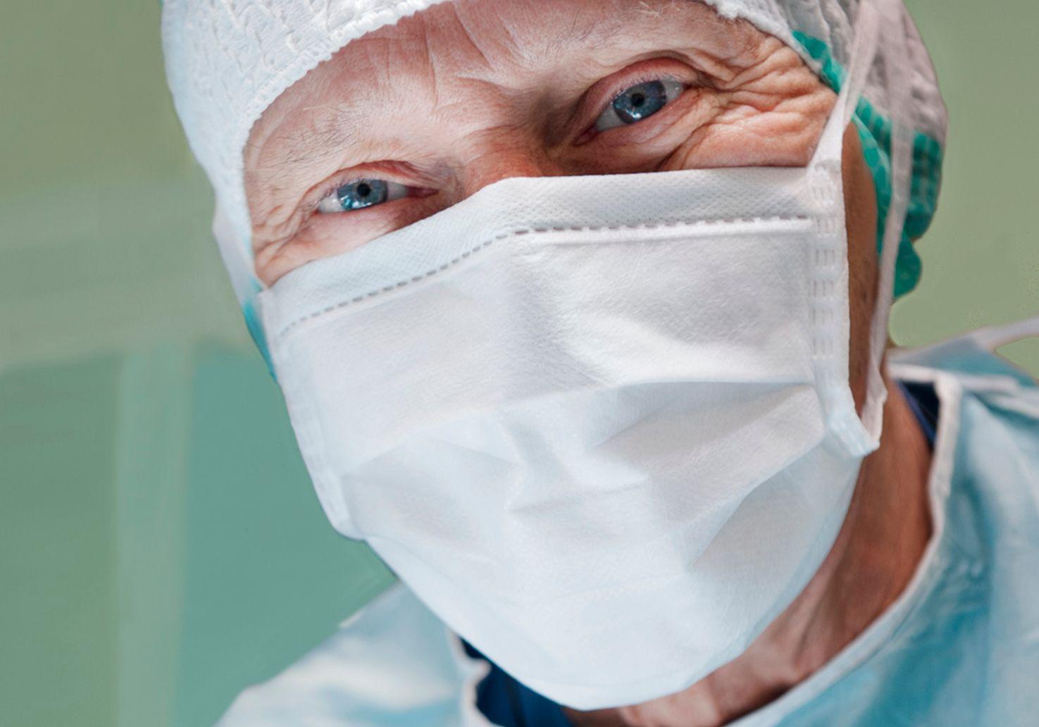 En manlig kirurg med mössa och munskydd. Han tittar rakt in i kameran.