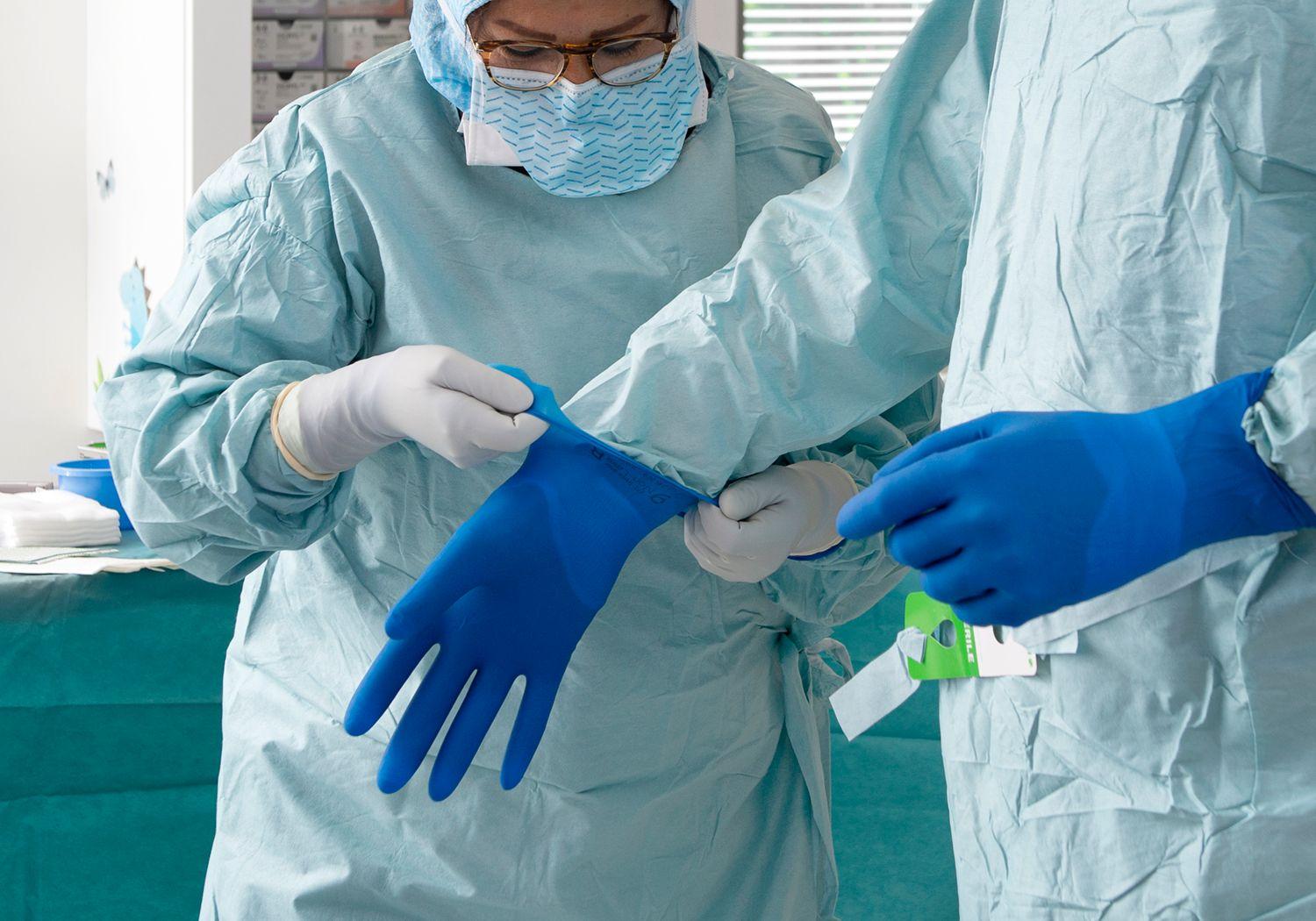 Sjuksköterska hjälper doktor att ta på sig rena, blå operationshandskar.