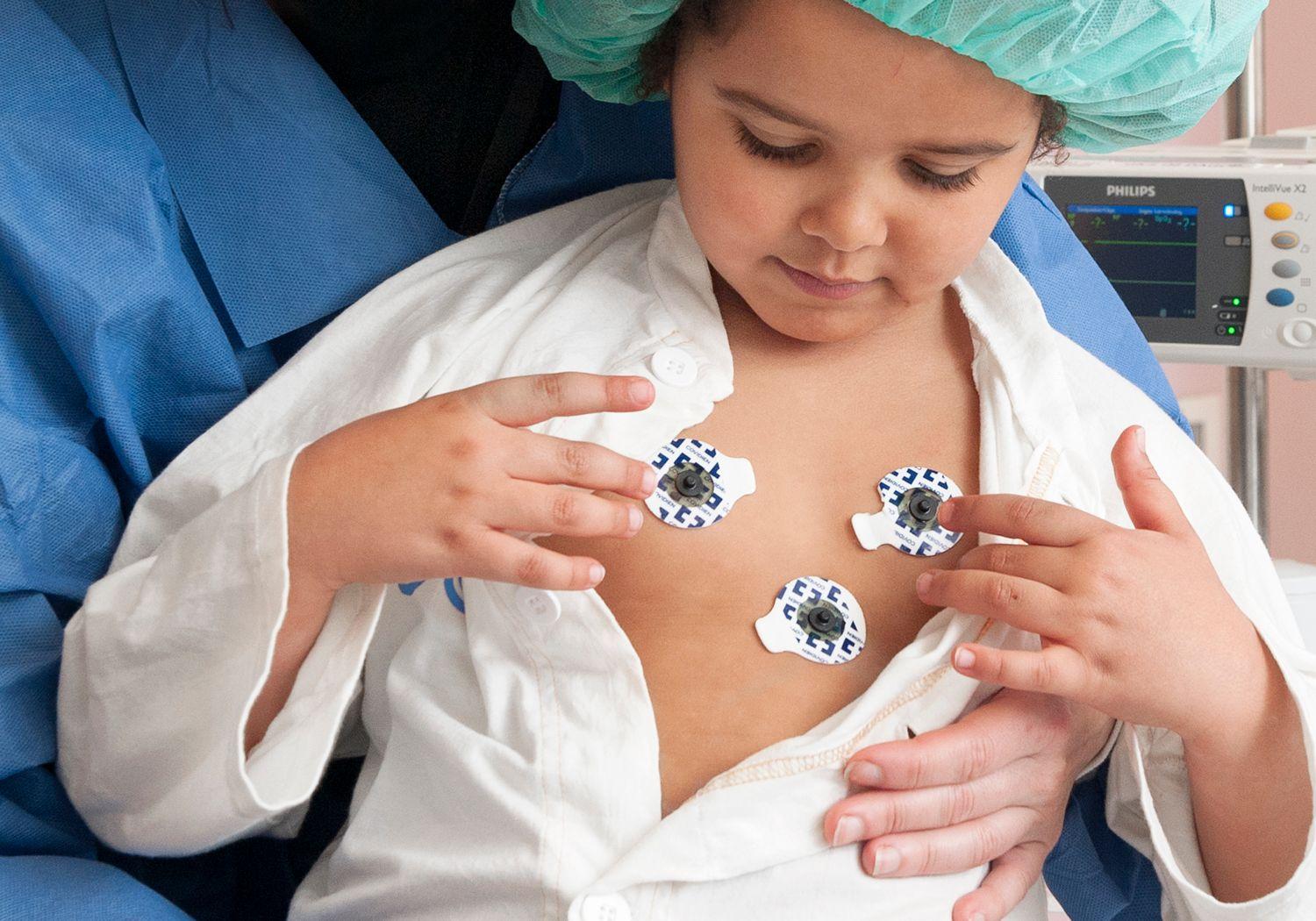 Flicka med tre klisterlappar för hjärtövervakning på bröstet.