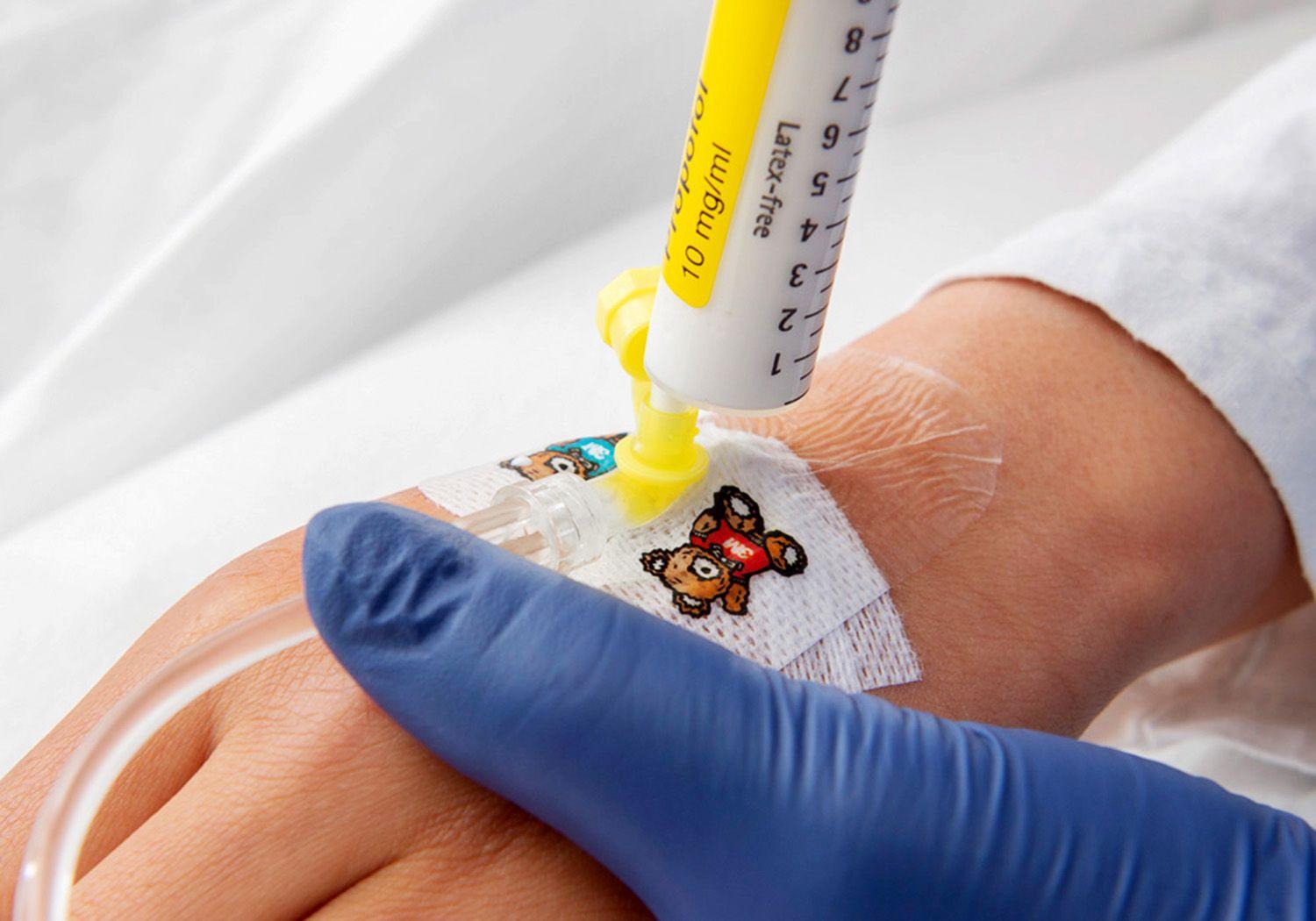 Sjuksköterska ger medicin med en spruta i en plastslang på en hand.
