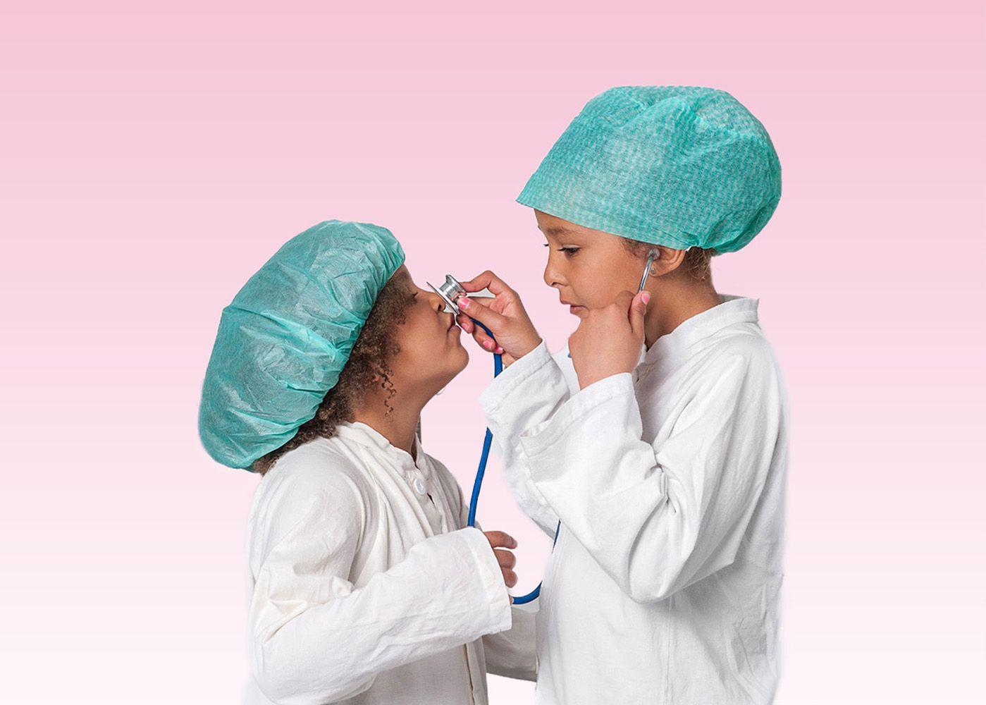 Två flickor i gröna operationsmössor står vända emot varann. Den ena flickan lyssnar på den andra flickans näsa med ett blått stetoskop.