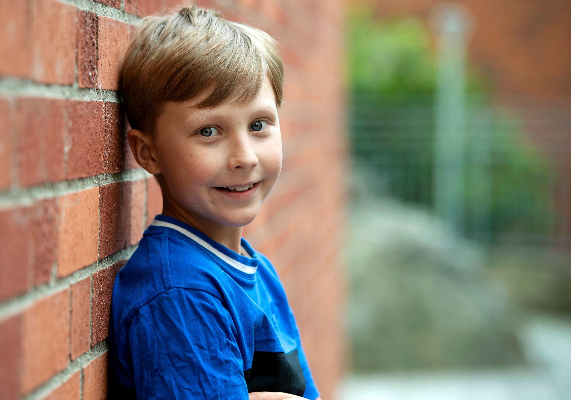 Frank, 9 år, står lutad mot en tegelvägg och ser glad ut.