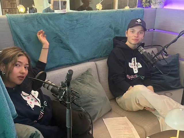 Två ungdomar, en kille och en tjej, sitter i en soffa under en podcastinspelning.