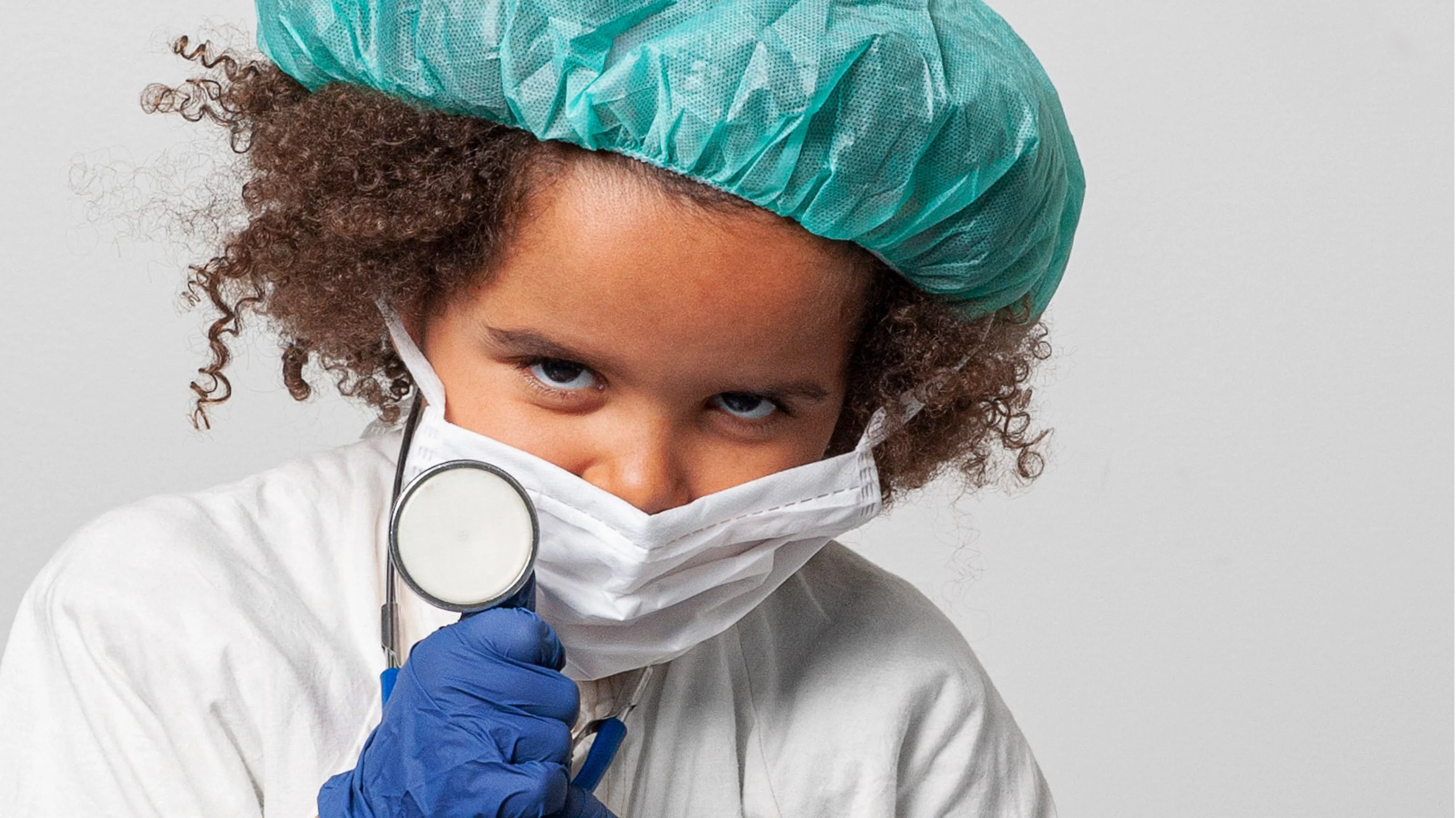 Flicka med mörkt hår i grön operationsmössa och munskydd.