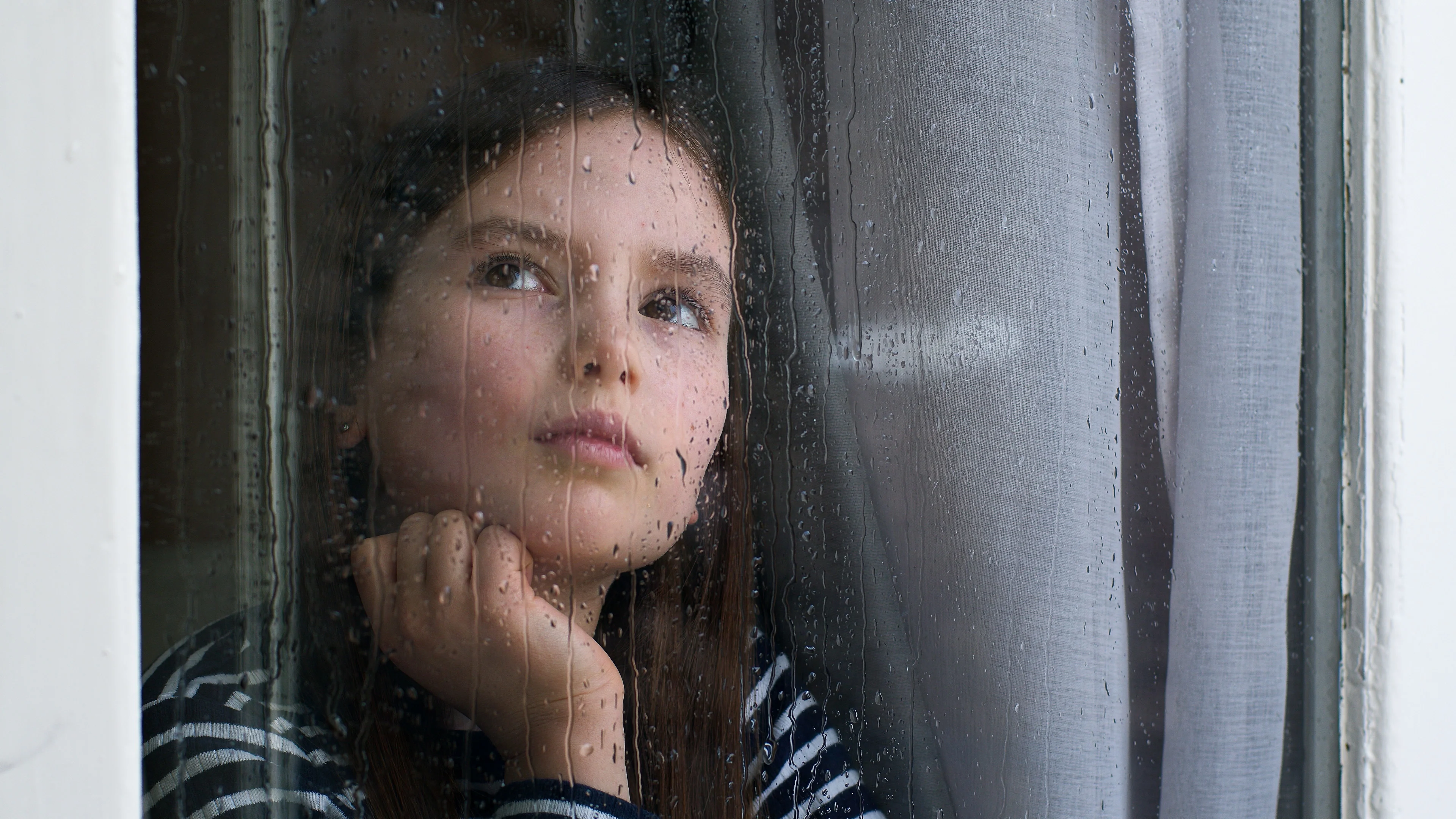 Flicka i mörkt hår tittar upp mot taket. Ser bekymrad ut.