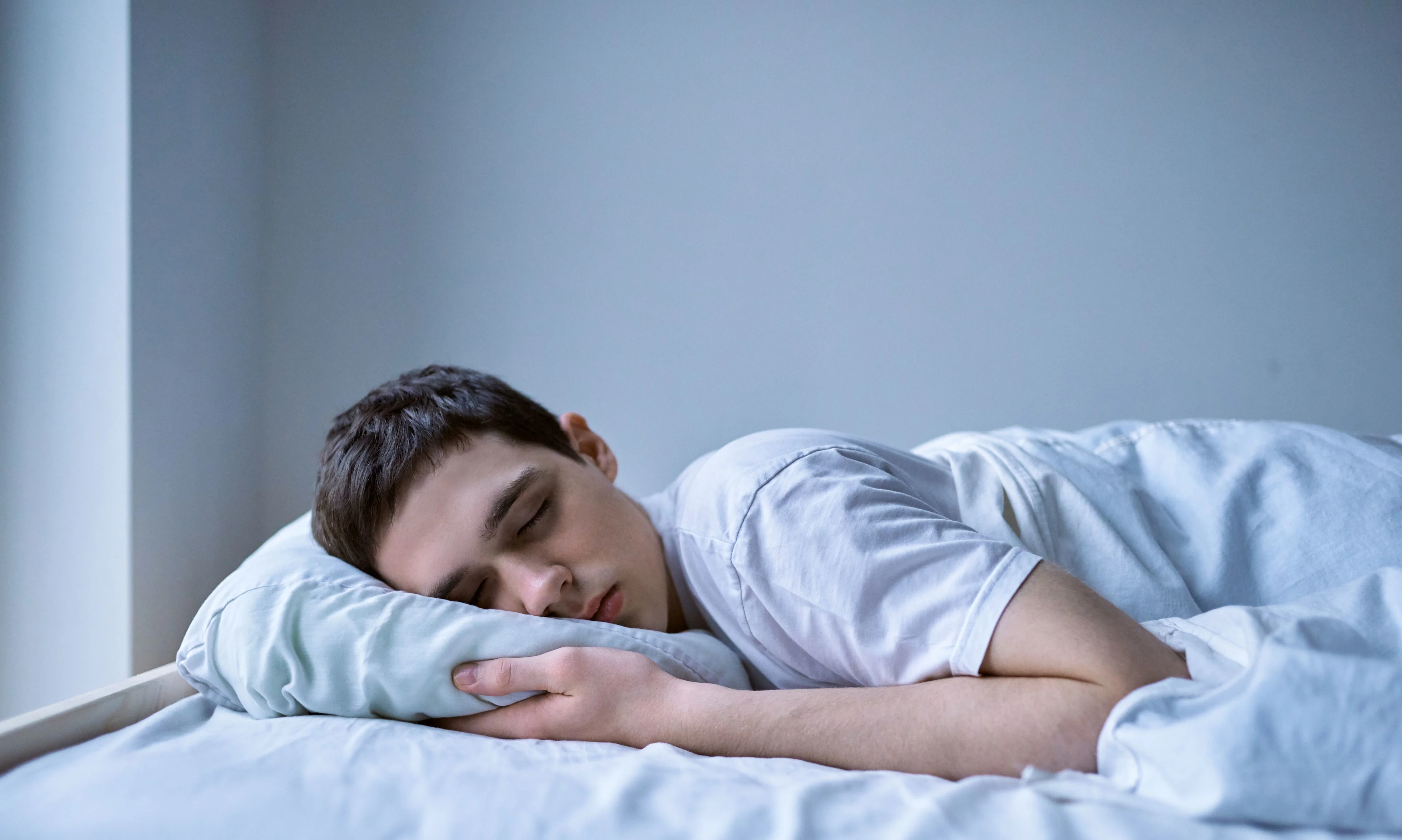 Tonårskille ligger på magen i sin säng. Sover.