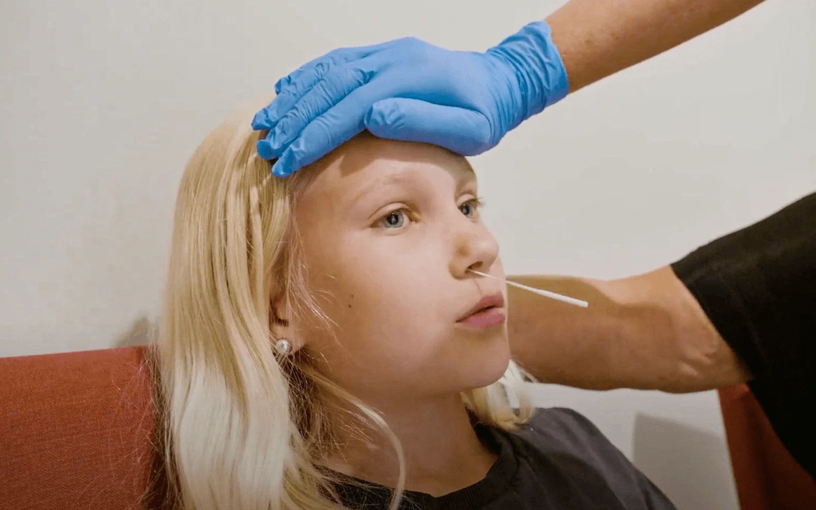 En flicka med ljust hår tar ett covidtest i näsan.