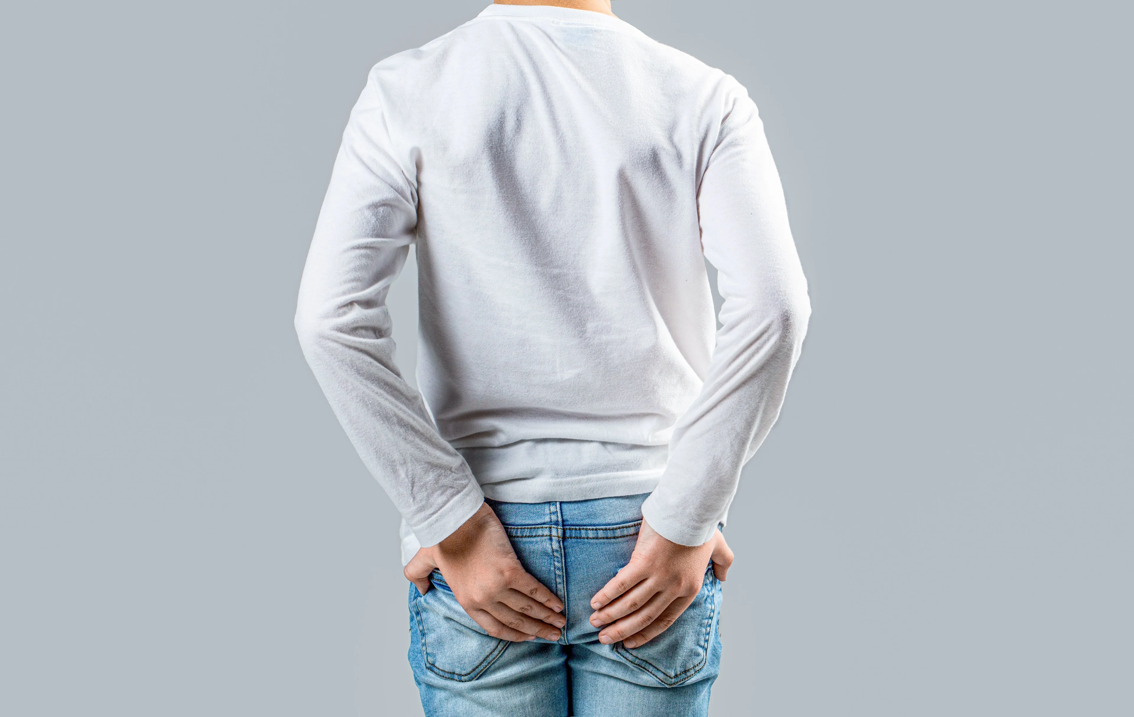 Tonårskille i ljus tröja och jeans håller händerna på bak-stjärten.