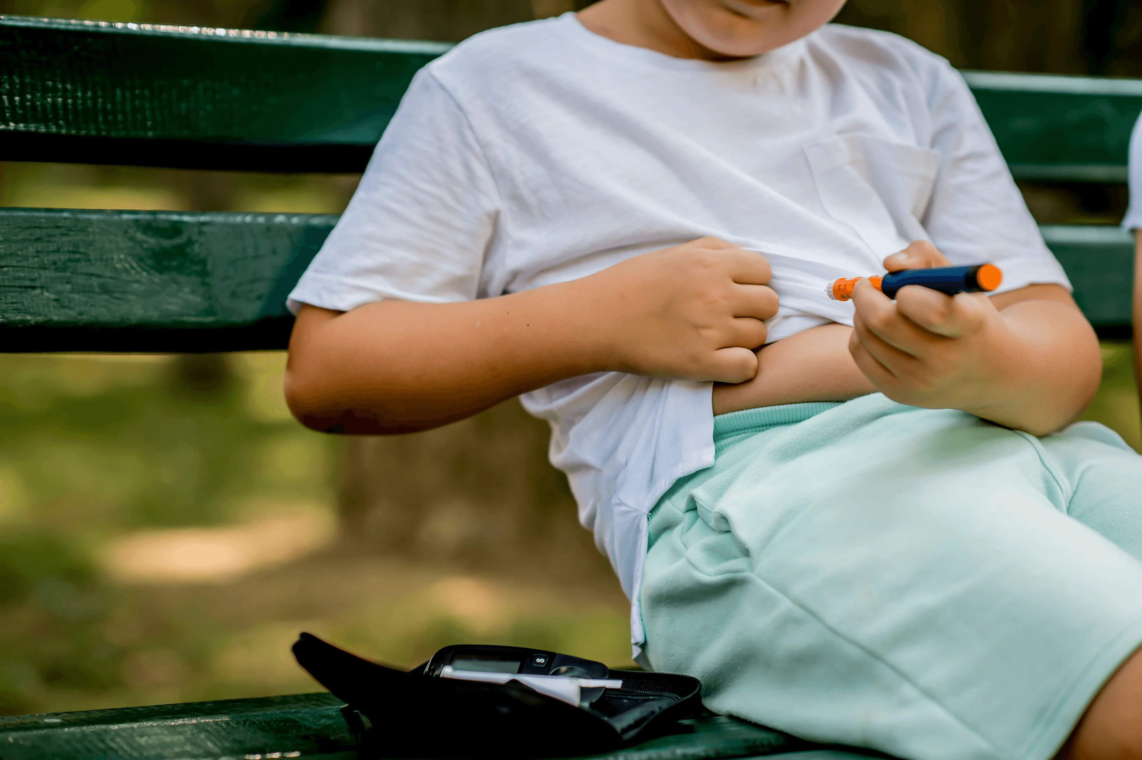 Pojke sitter på en parkbänk. Ger sig själv en spruta med insulin i mage.