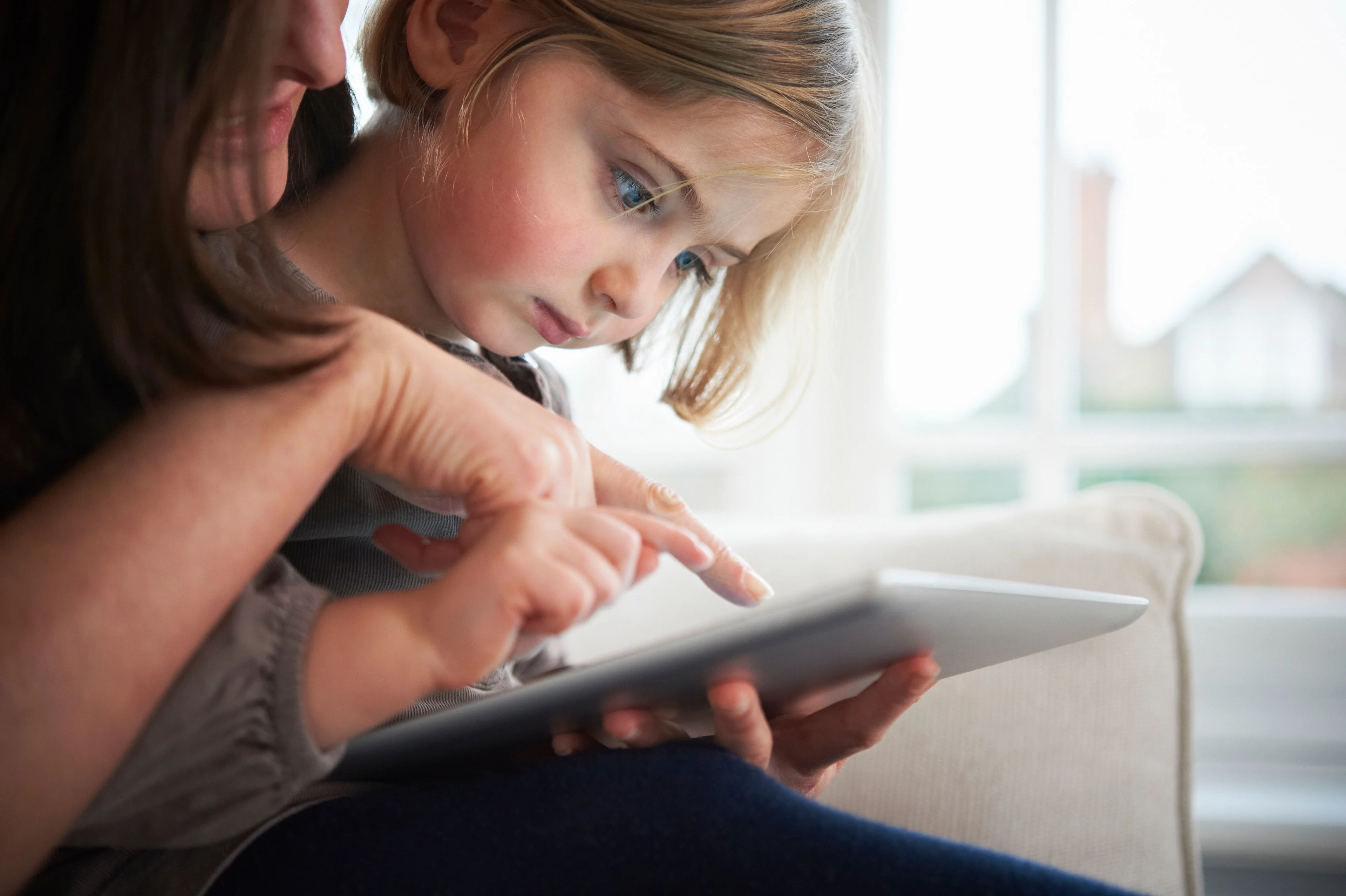 Närbild på en flicka och en vuxen kvinna som tillsammans tittar på en IPad.