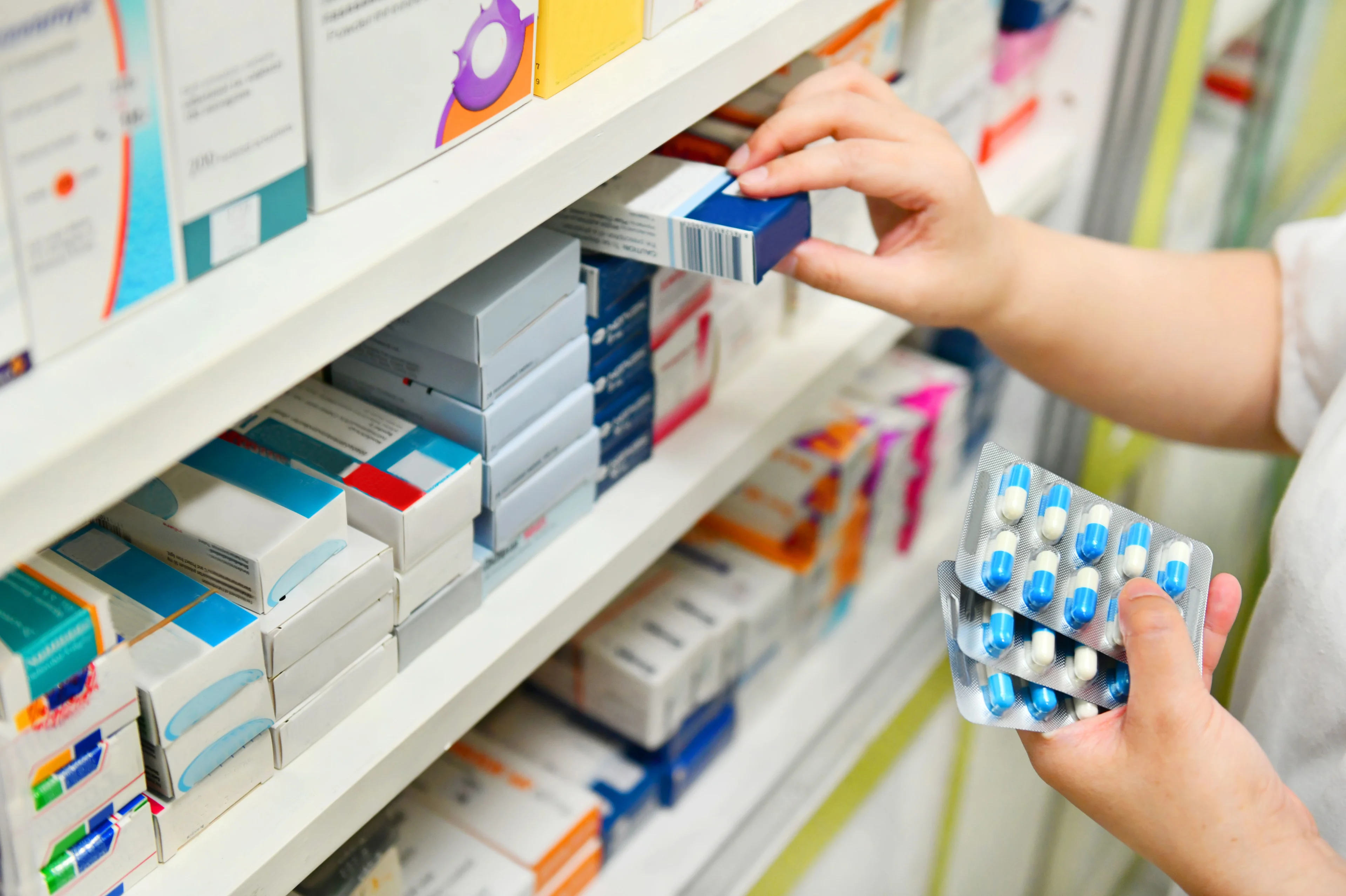 Närbild på en hylla på ett apotek. Många förpackningar med medicin. En person plockar med förpackningarna.