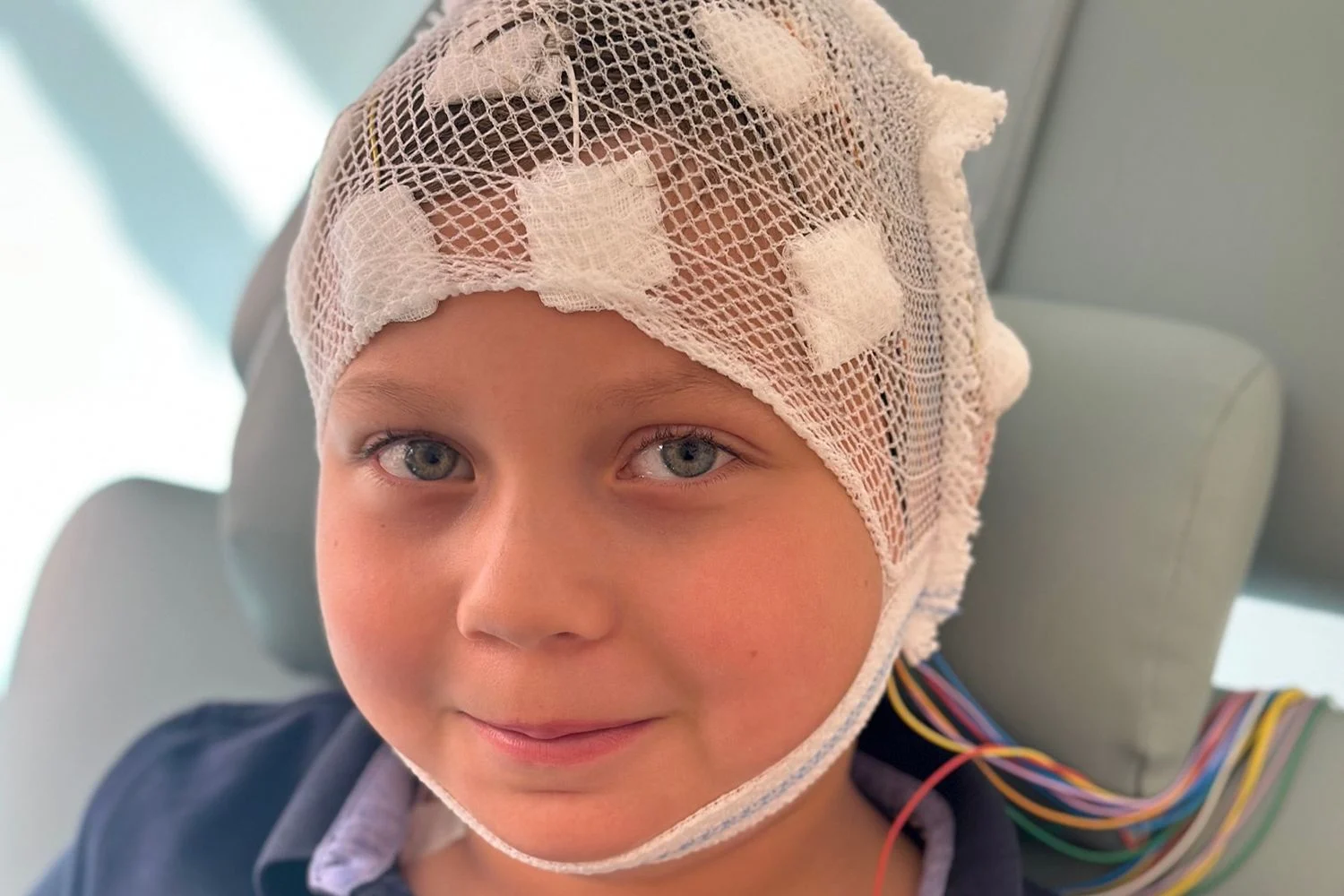 En pojke med epilepsi genomgår en EEG-undersökning. Han har en kompresser, sladdar och en genomskinlig mössa på huvudet.