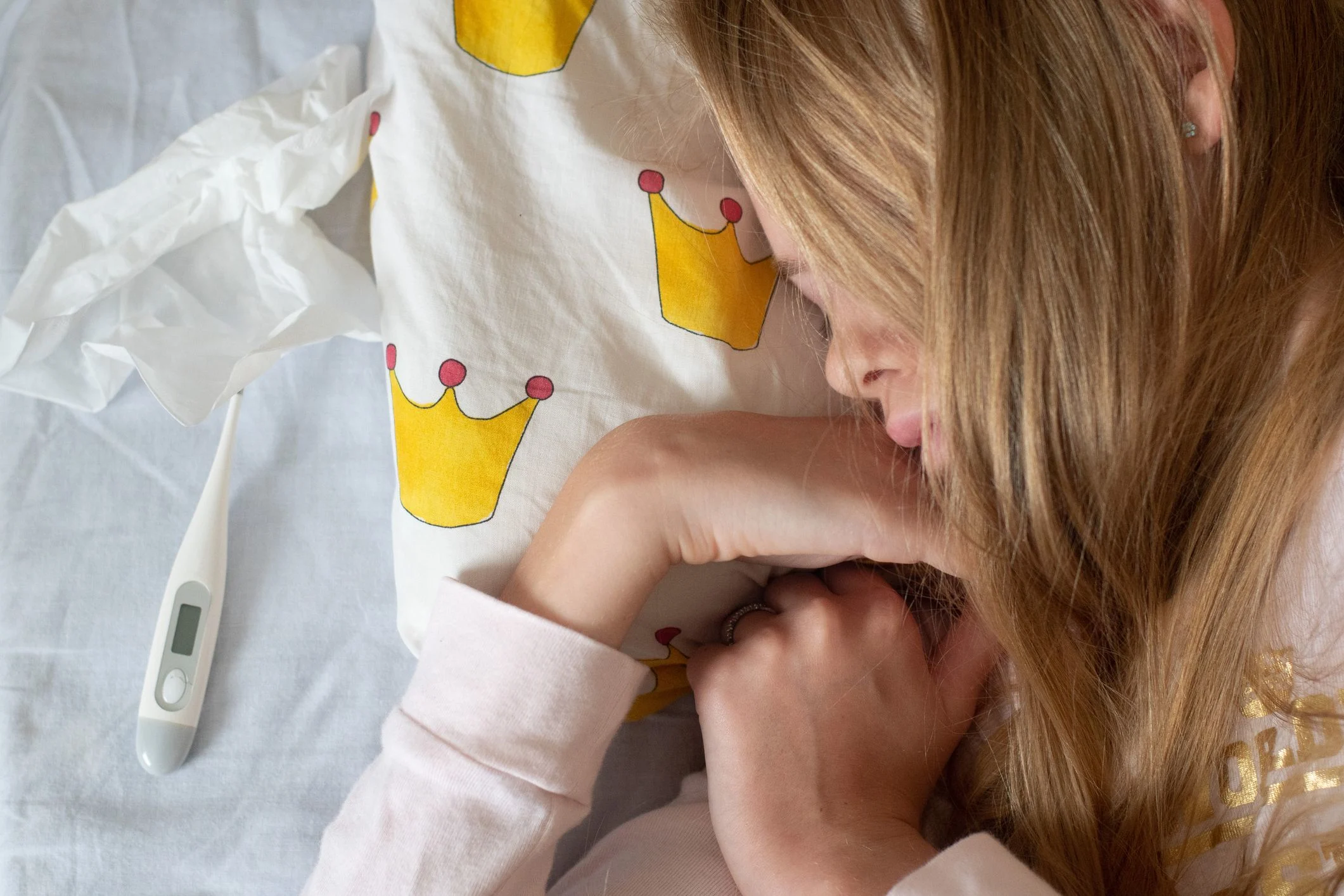 En flicka ligger på sidan i sin säng. Flickan sover. En febertermometer ligger bredvid henne på kudden.