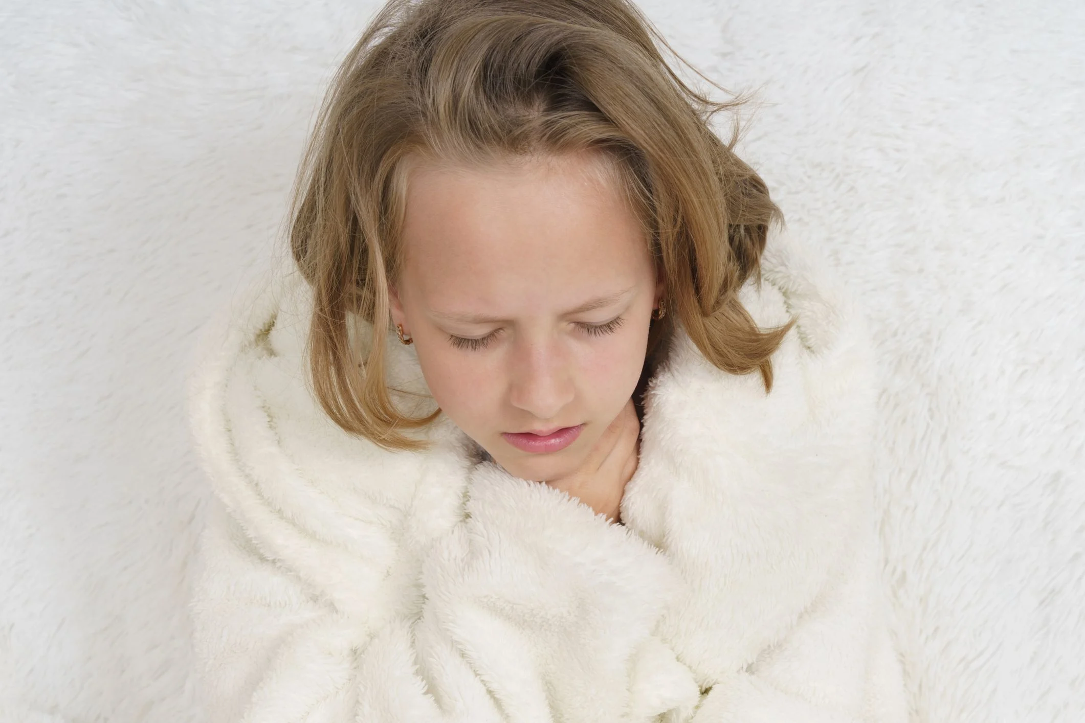 En flicka i vit morgonrock håller sig för halsen och grinar illa.