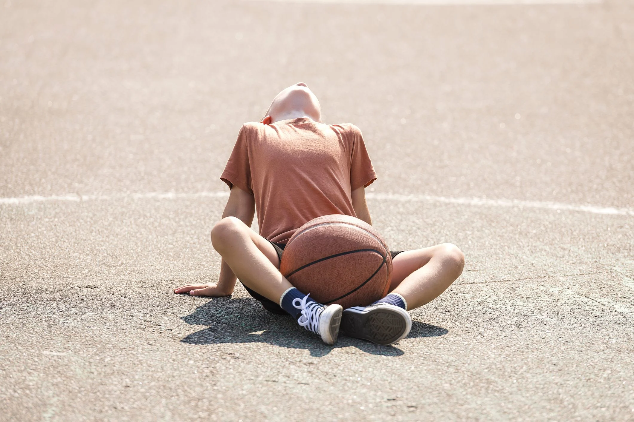 Pojke i brun t-shirt sitter på marken. Trött efter en basket match.