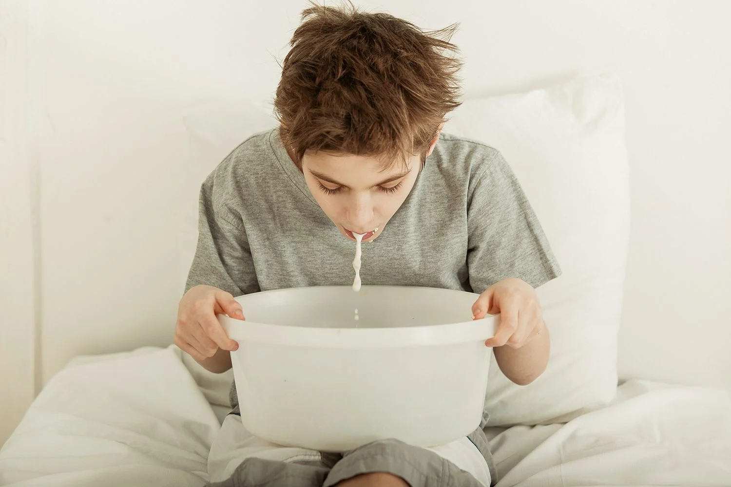 En pojke i en grå t-shirt kräks i en hink.