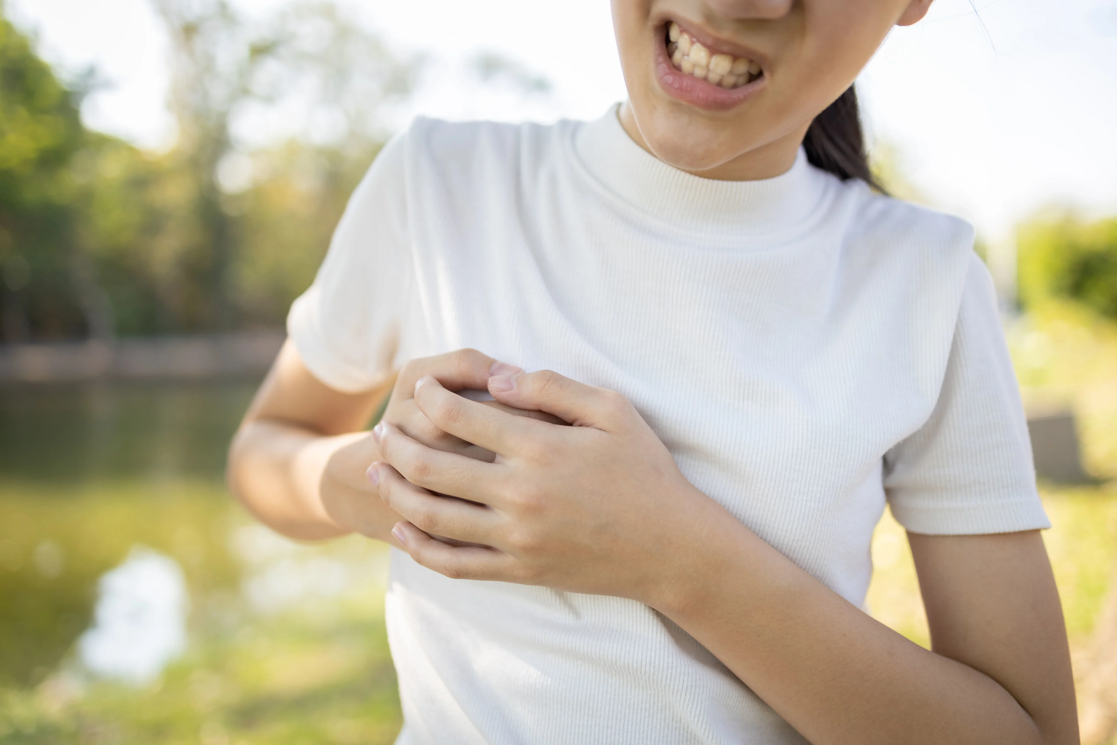 En flicka i vit t-shirt tar sig för höger bröstkorg. Grinar illa och ser ut att ha ont.