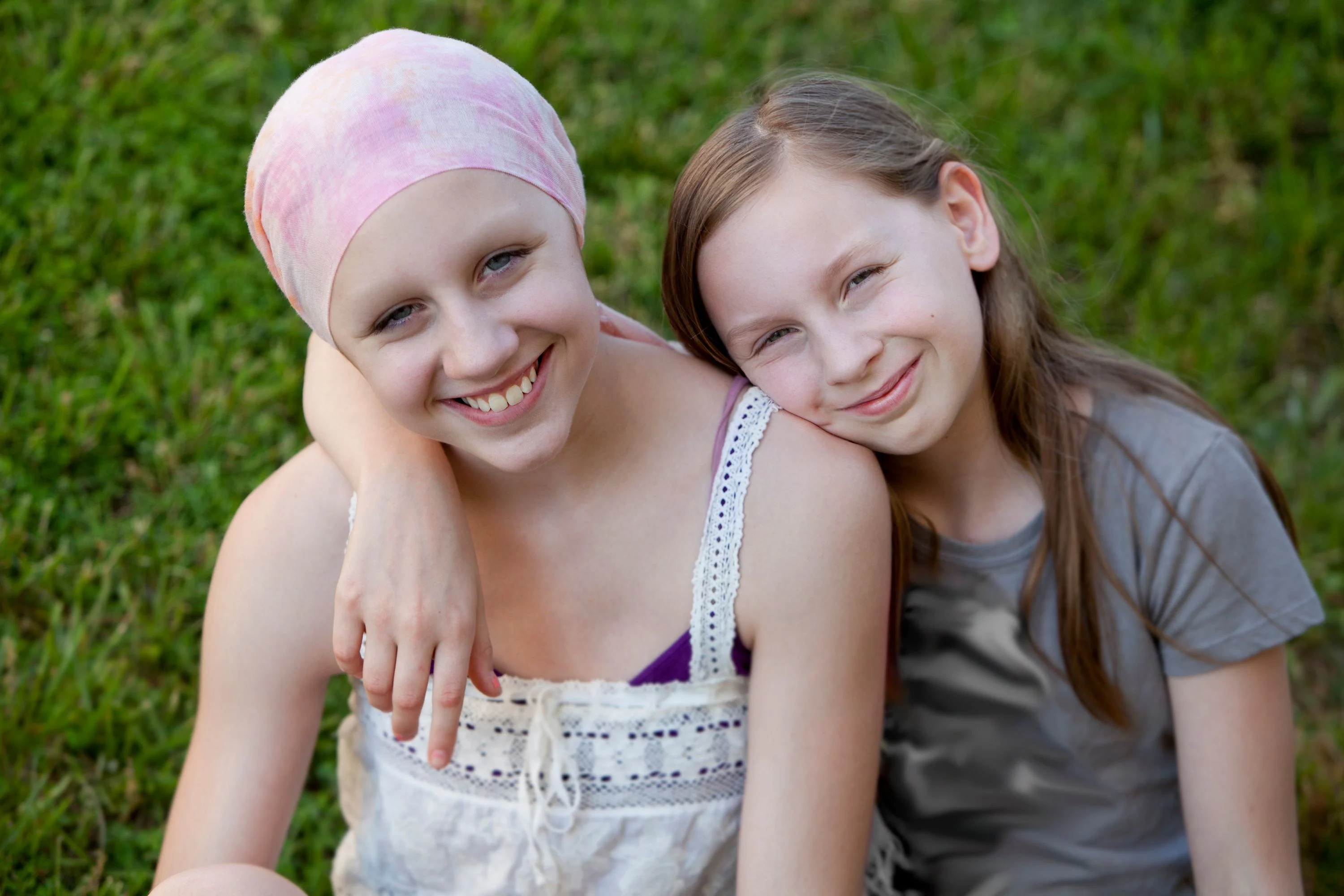 En flicka håller armen om en annan flicka som har en rosa scharl på huvudet.