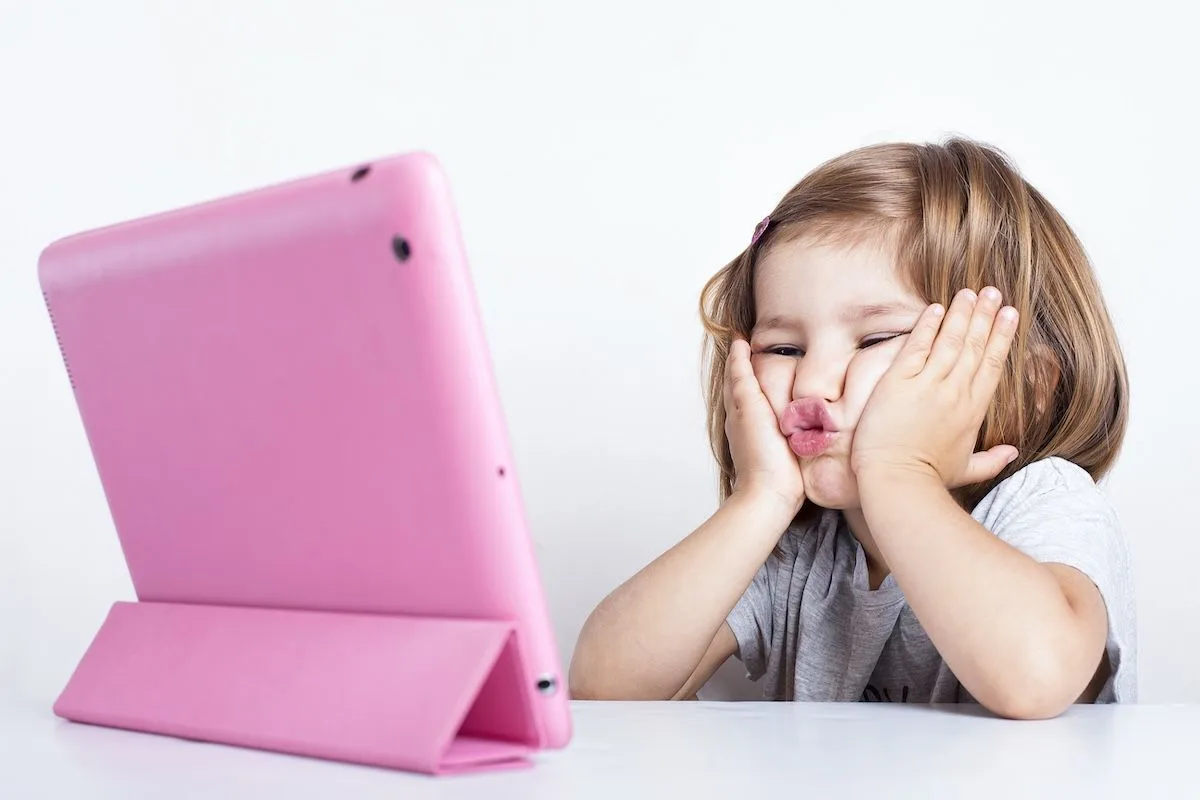 En flicka håller händerna på sina kinder. Tittar på en Ipad med rosa fodral.