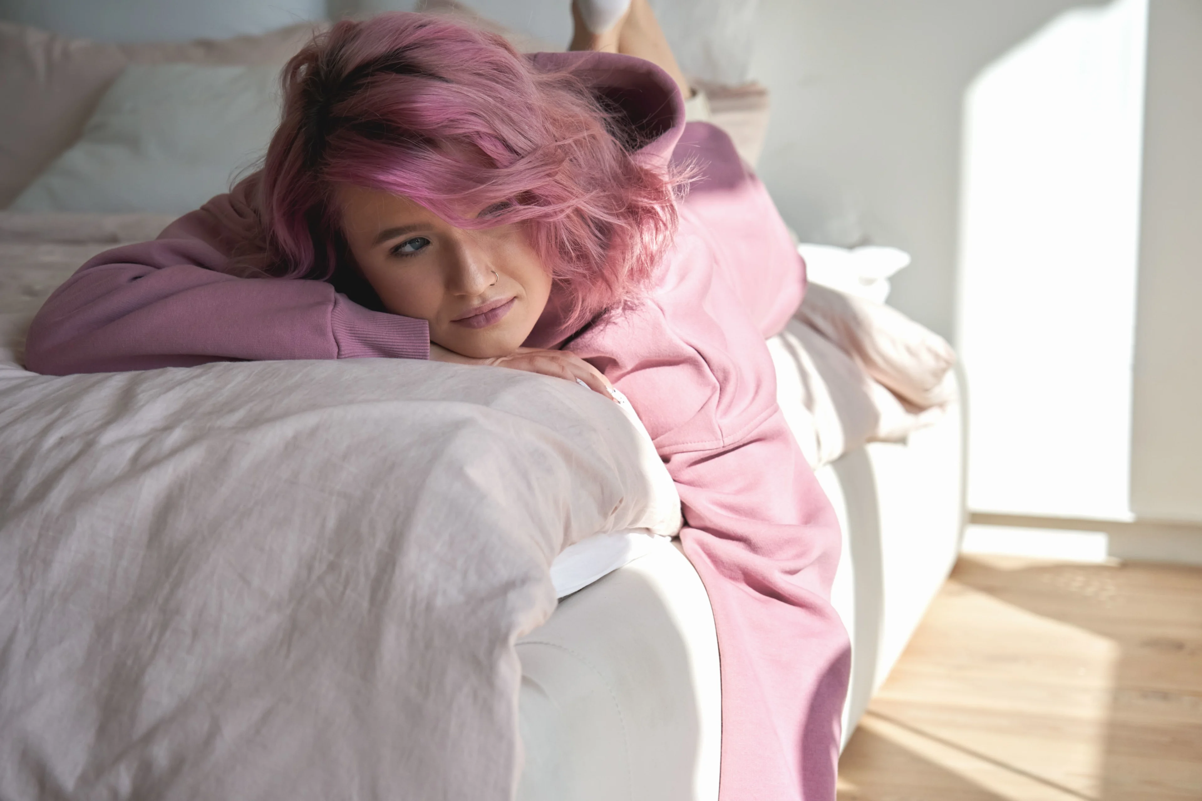 Flicka med rosa hår och rosa hoodie ligger på magen i sin säng och funderar.