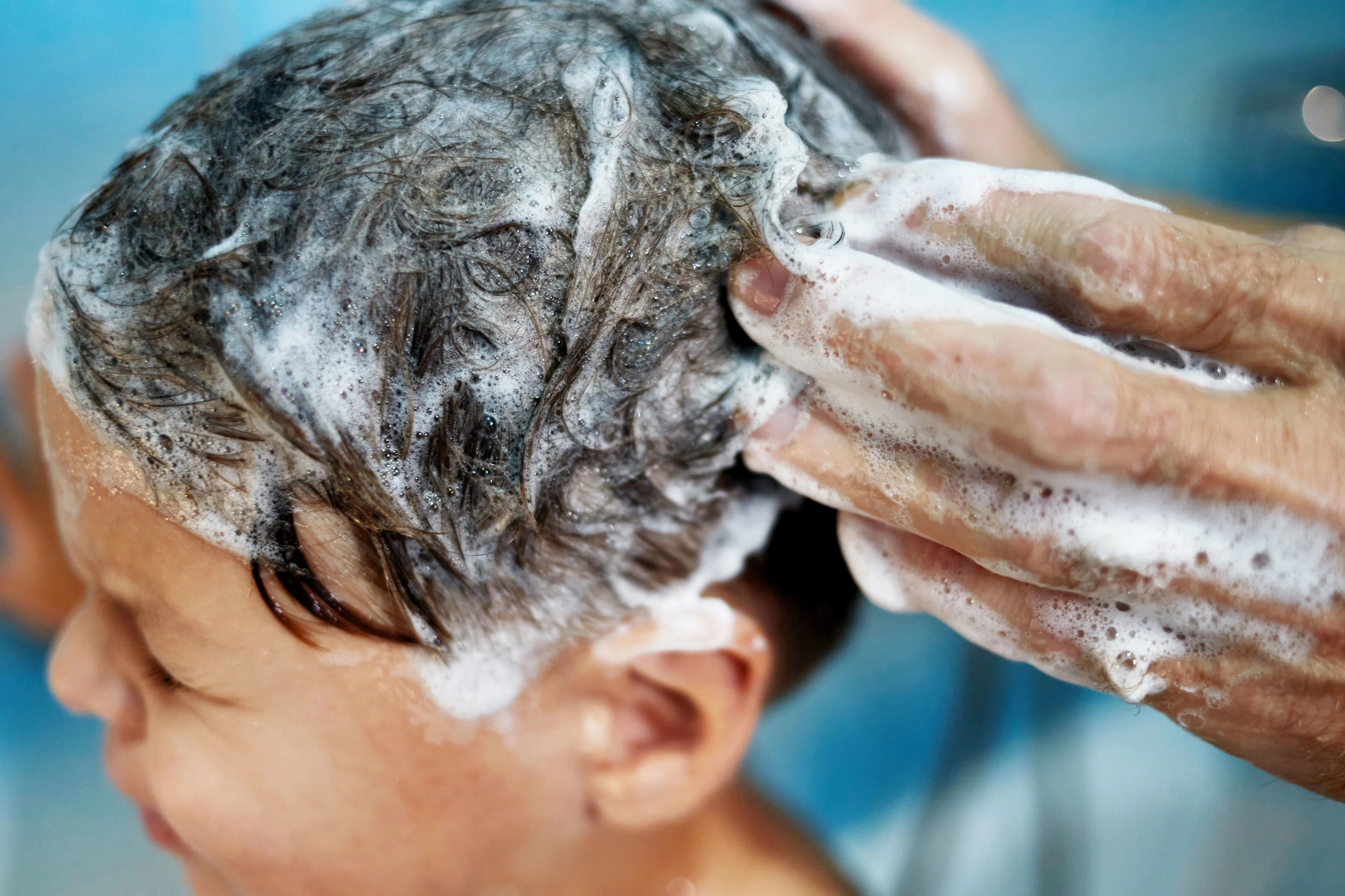 Ett barn får hjälp att tvätta håret. Det löddrar mycket från shampoo.