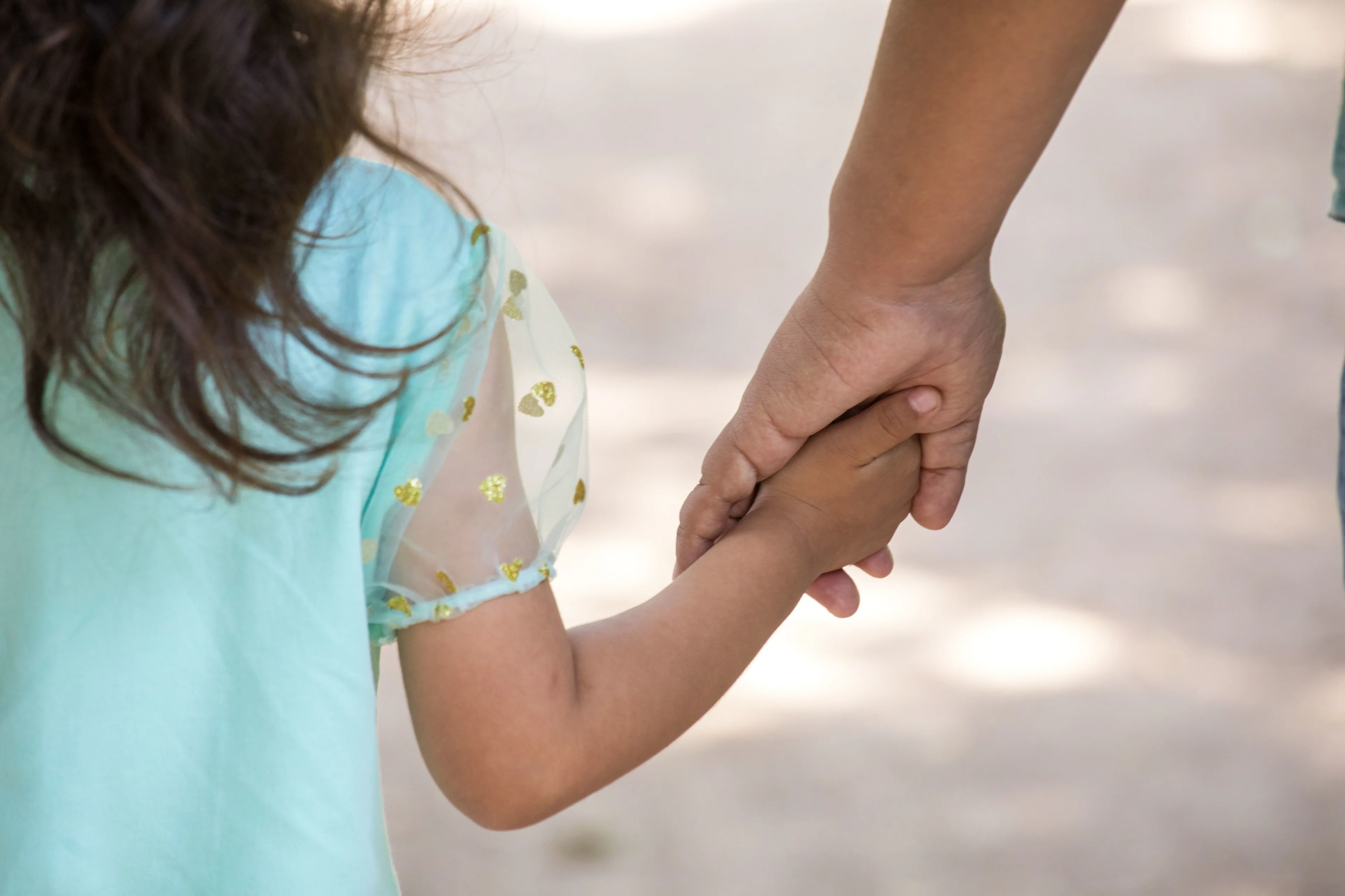 Pappa håller en flicka i handen. Flickan har mörkt hår och en turkos tröja på sig.
