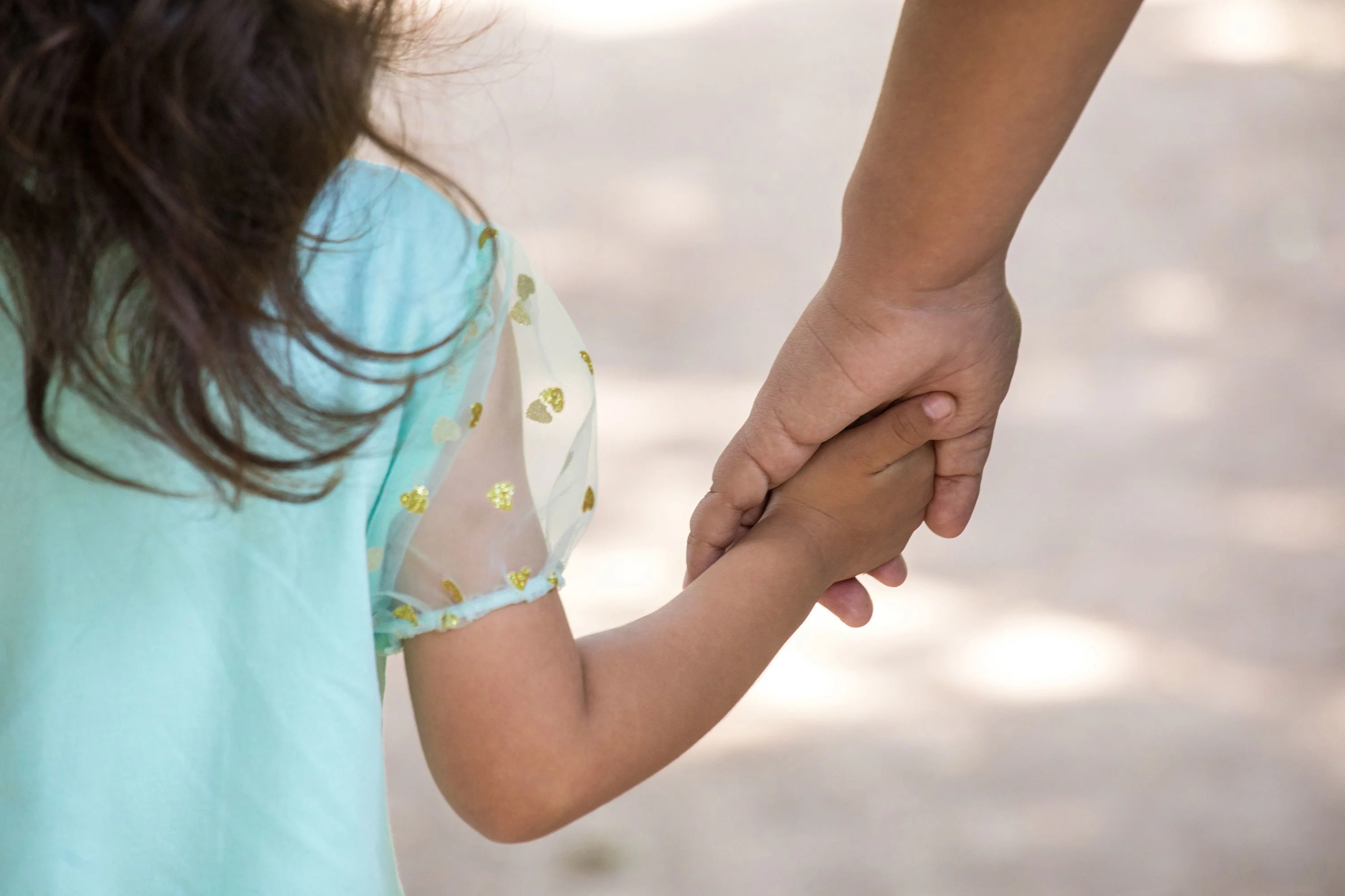 Pappa håller en flicka i handen. Flickan har mörkt hår och en turkos tröja på sig.