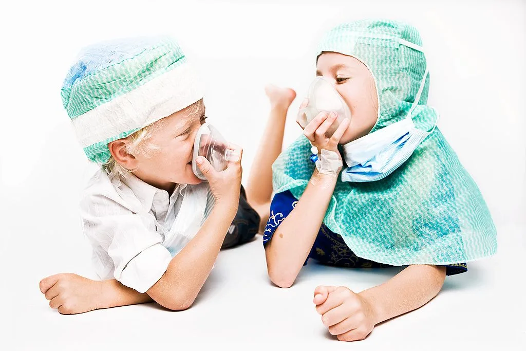 Girl and boy in scrub caps lie on their stomachs, each breathing in an oxygen mask.