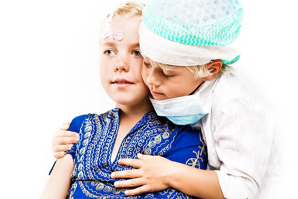 Liten pojke i operationsmössa håller om en liten flicka i blå skjorta.
