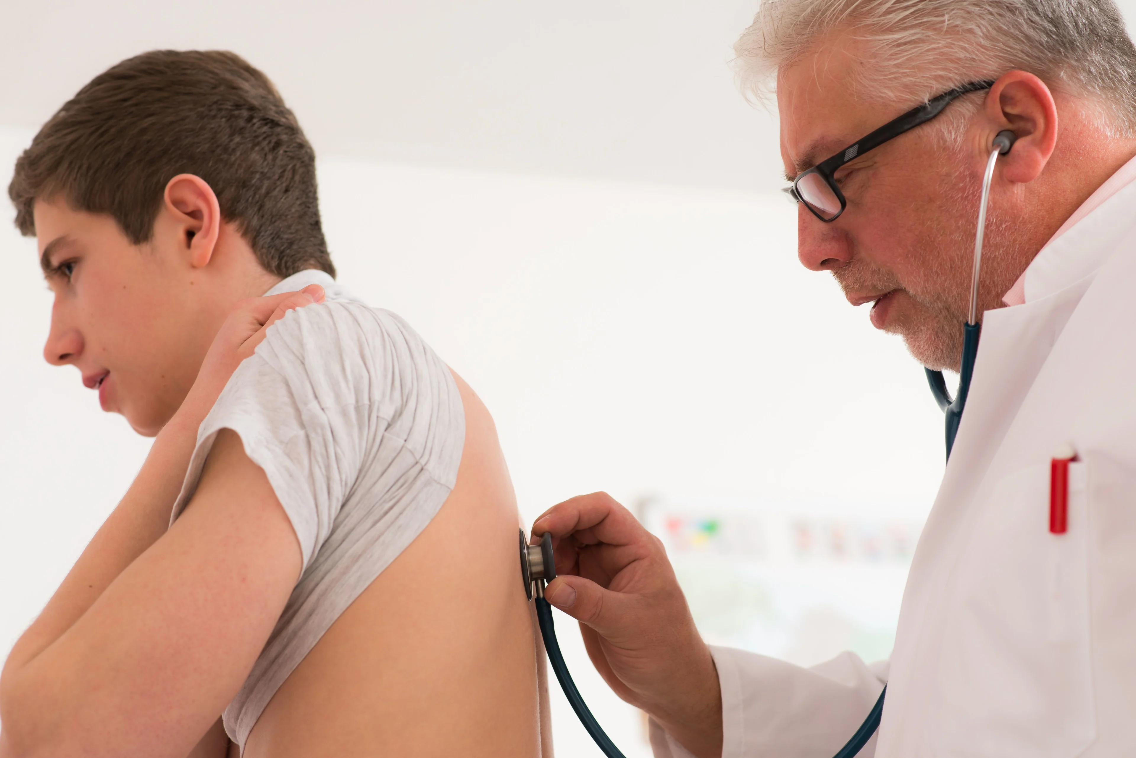 En doktor lyssnar på lungorna med ett stetoskop på ryggen på en tonårskille.