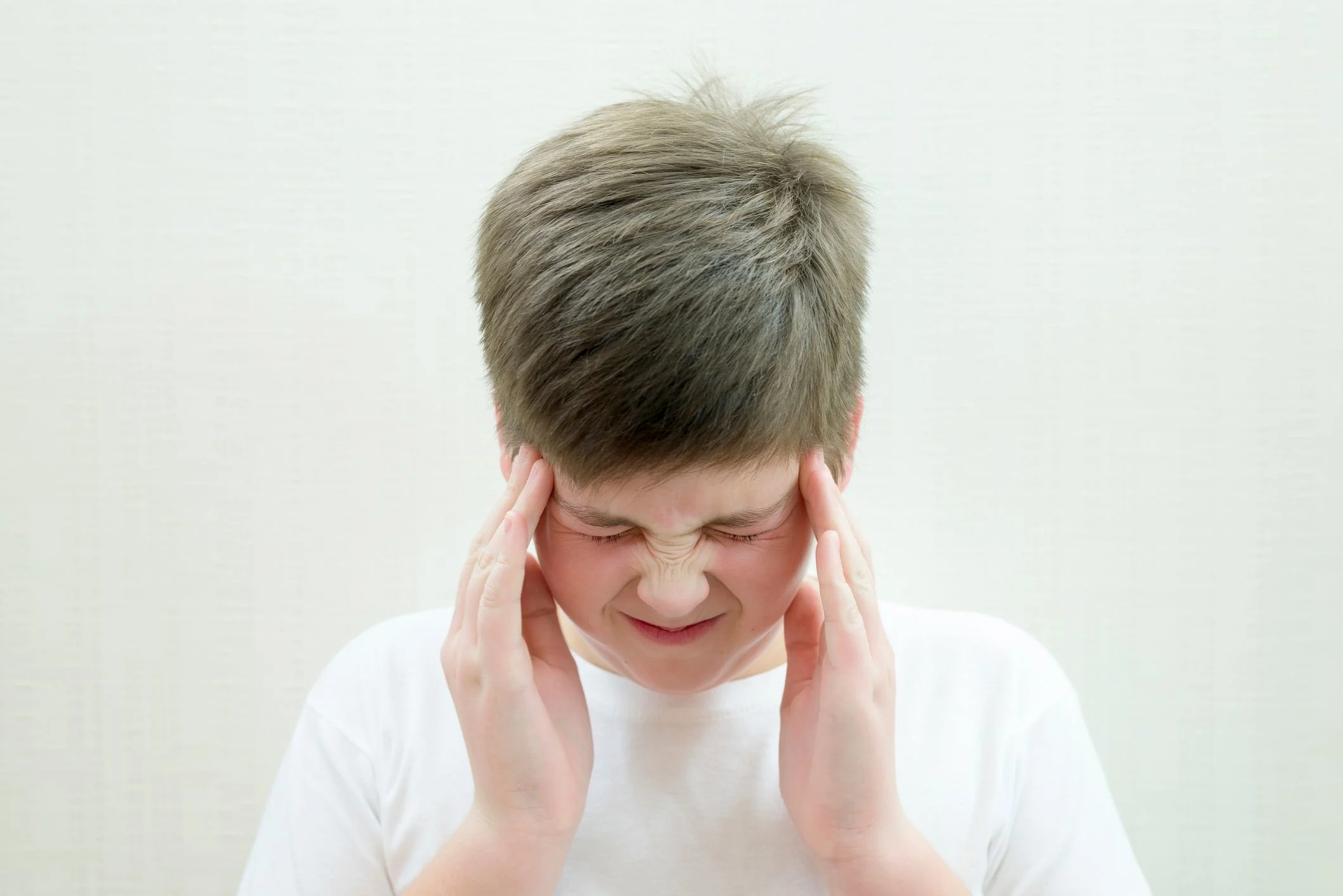 En pojke i vid t-shirt tar sig med händerna om huvudet.