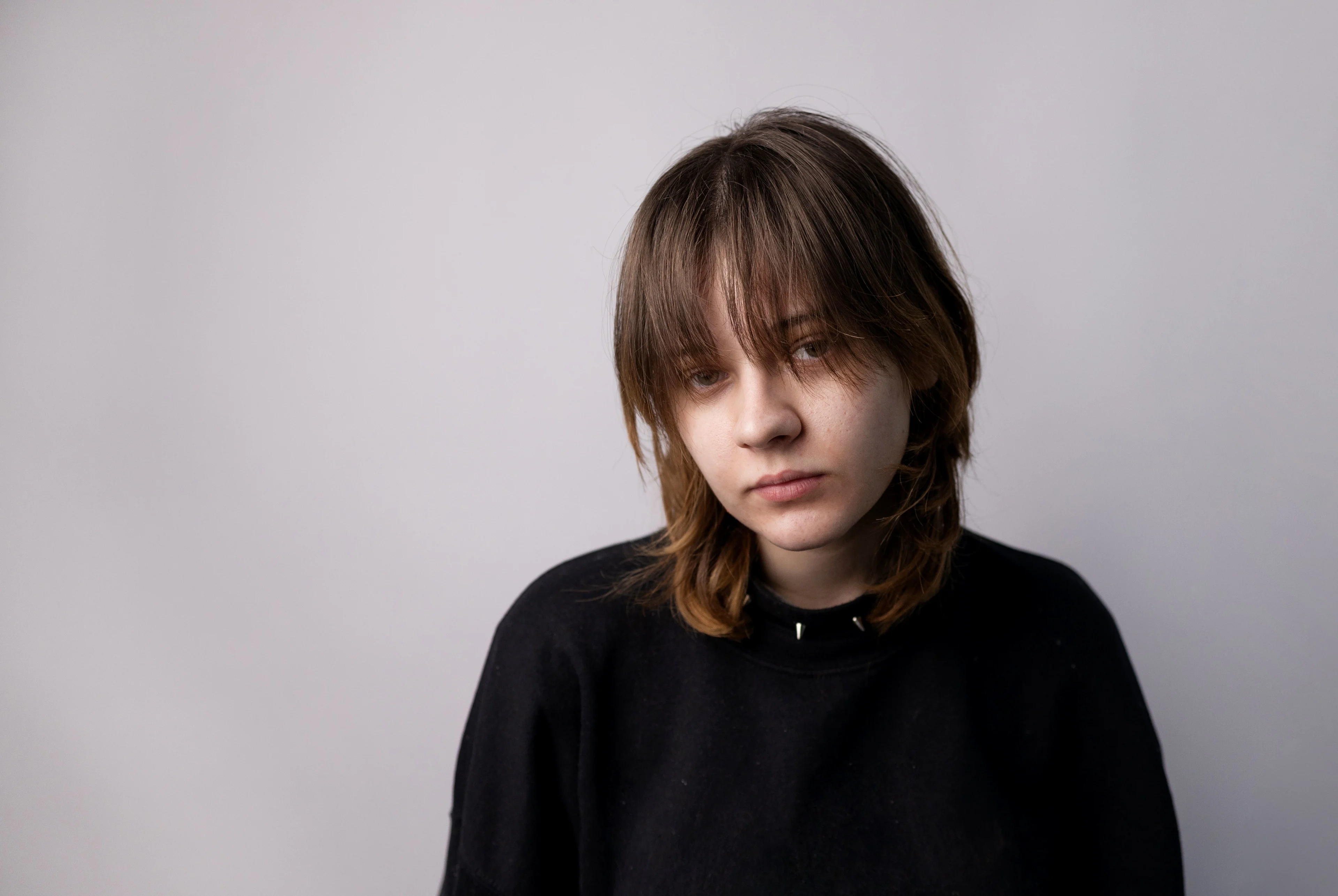 Tonårstjej med mörkt hår och svart tröja. Tittar in i kameran. Ser nedstämd ut.