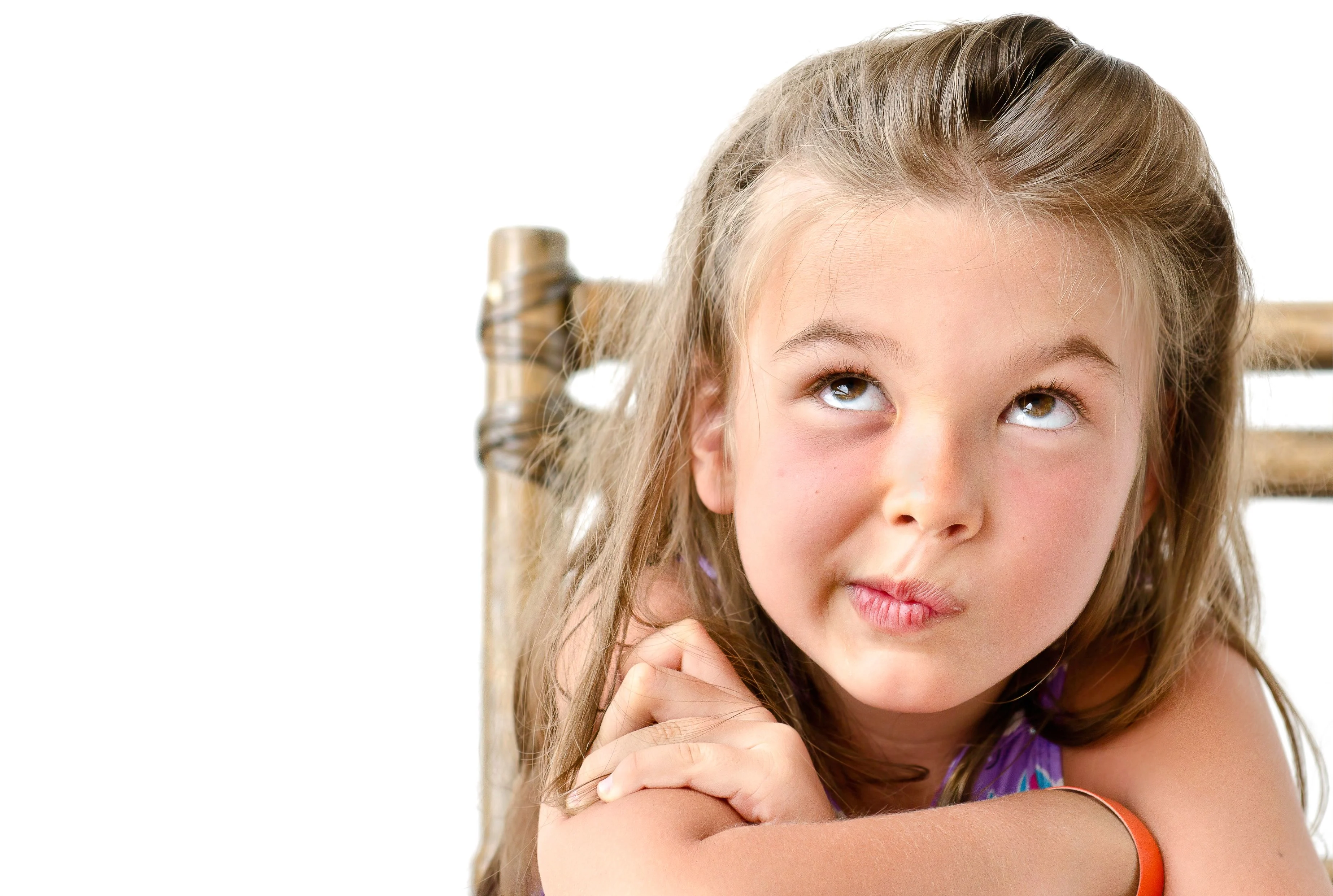 En skolflicka med långt hår sitter på en stol. Ser fundersam ut.