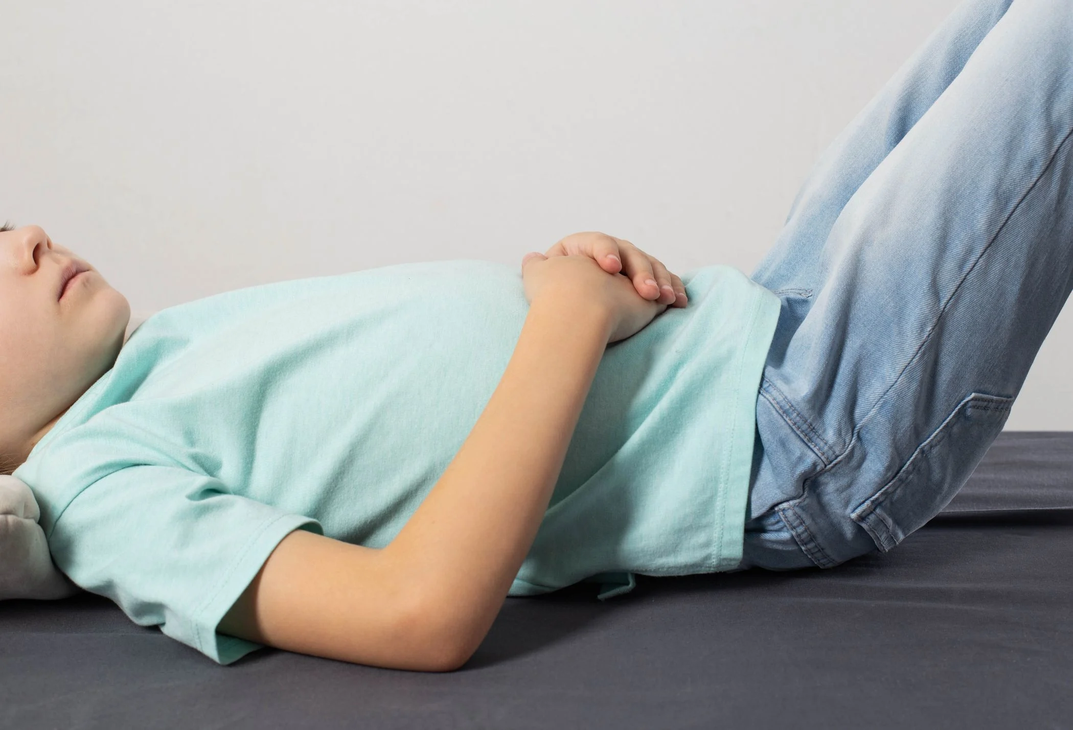 En liten pojke ligger på rygg med benen högt. Håller händerna för magen.