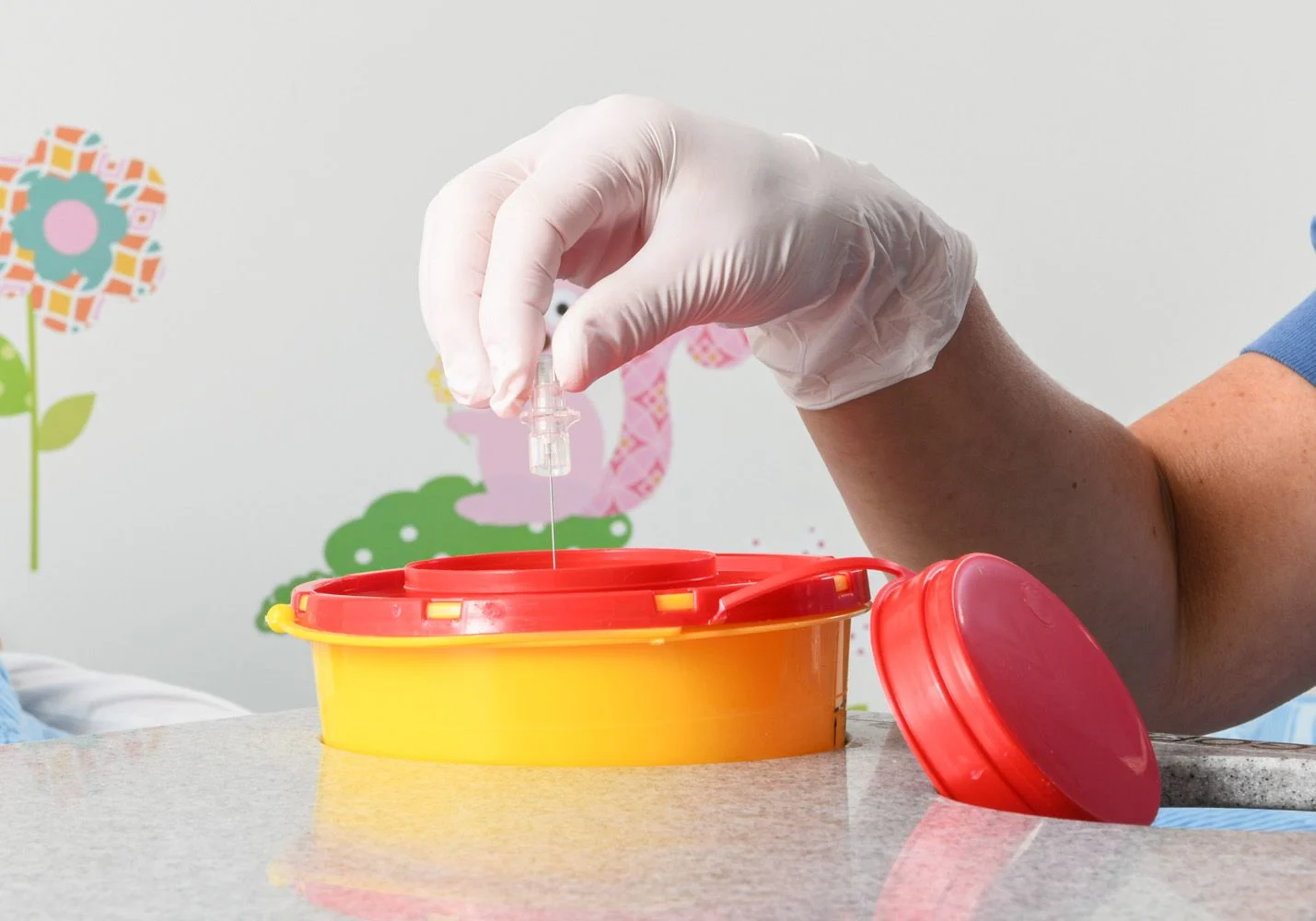 Lollo discards the needle in a little yellow bucket with a red lid.